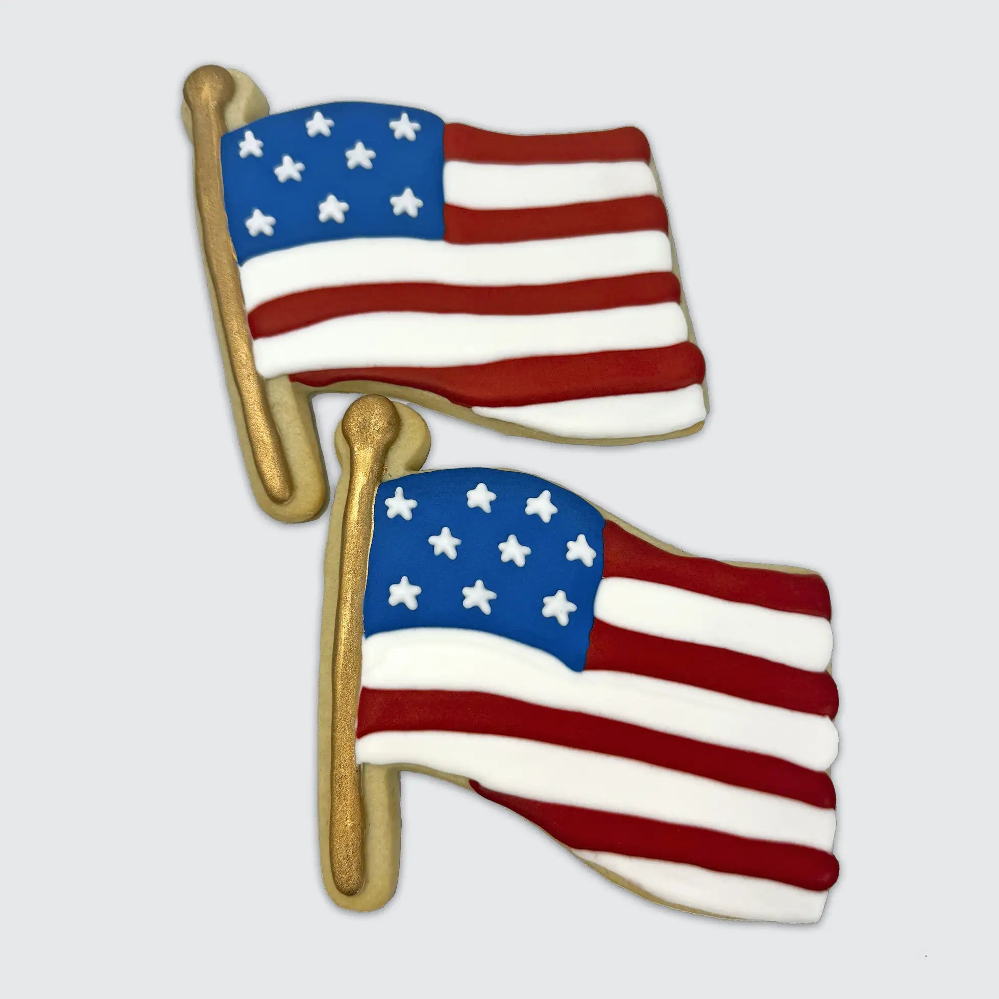 Two American flag-shaped cookies with red and white stripes, blue star field, and gold flagpole.