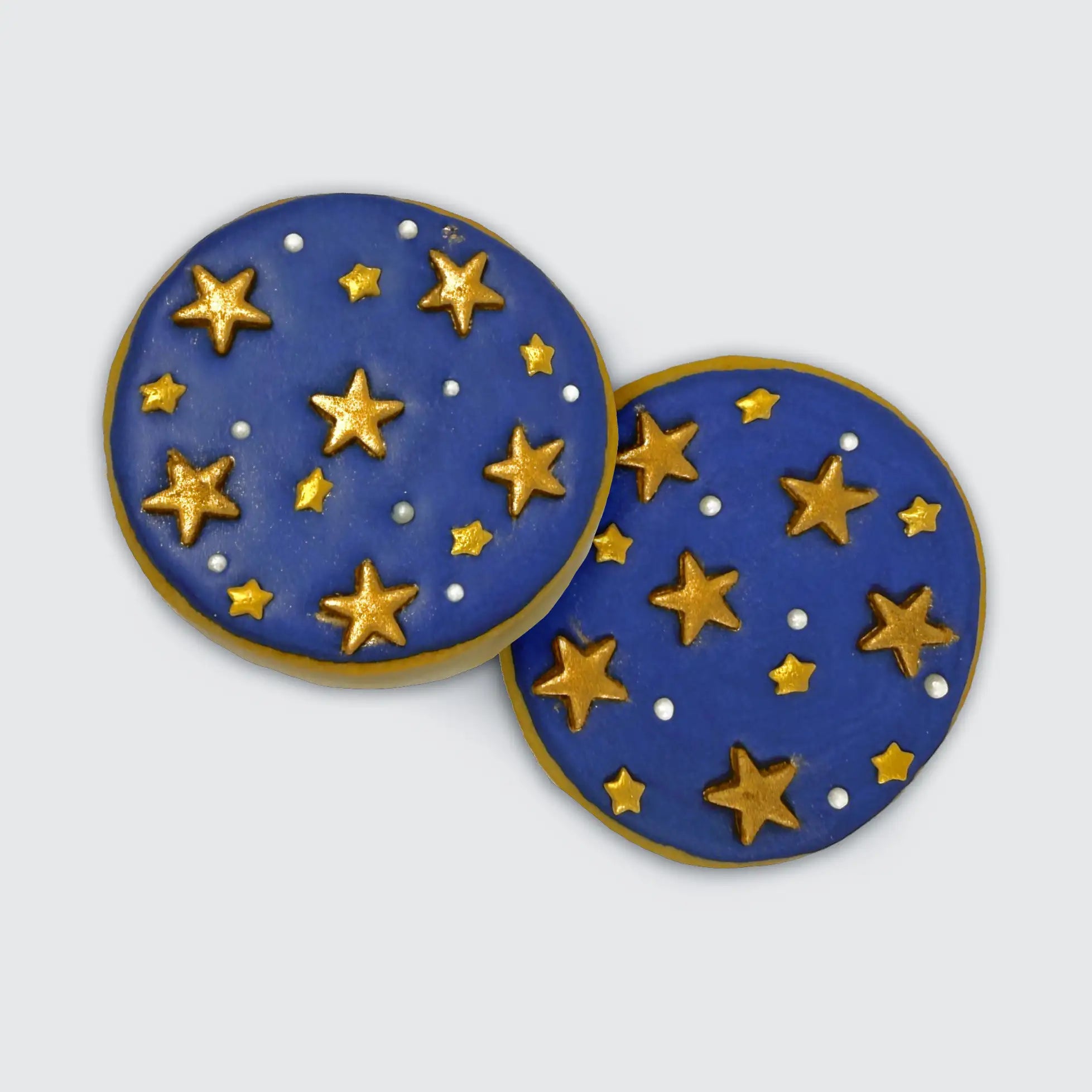 Two round cookies with blue icing topped with gold stars and silver dots, designed to look like a starry night sky.