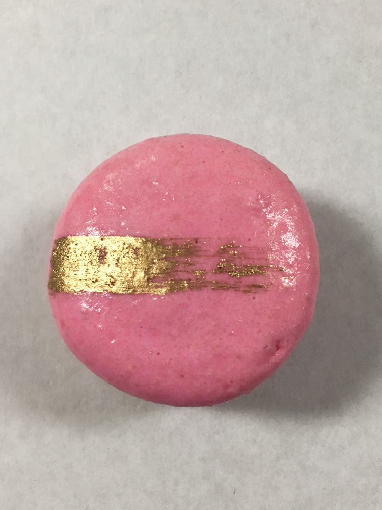 A pink macaron with a gold streak on its surface.
