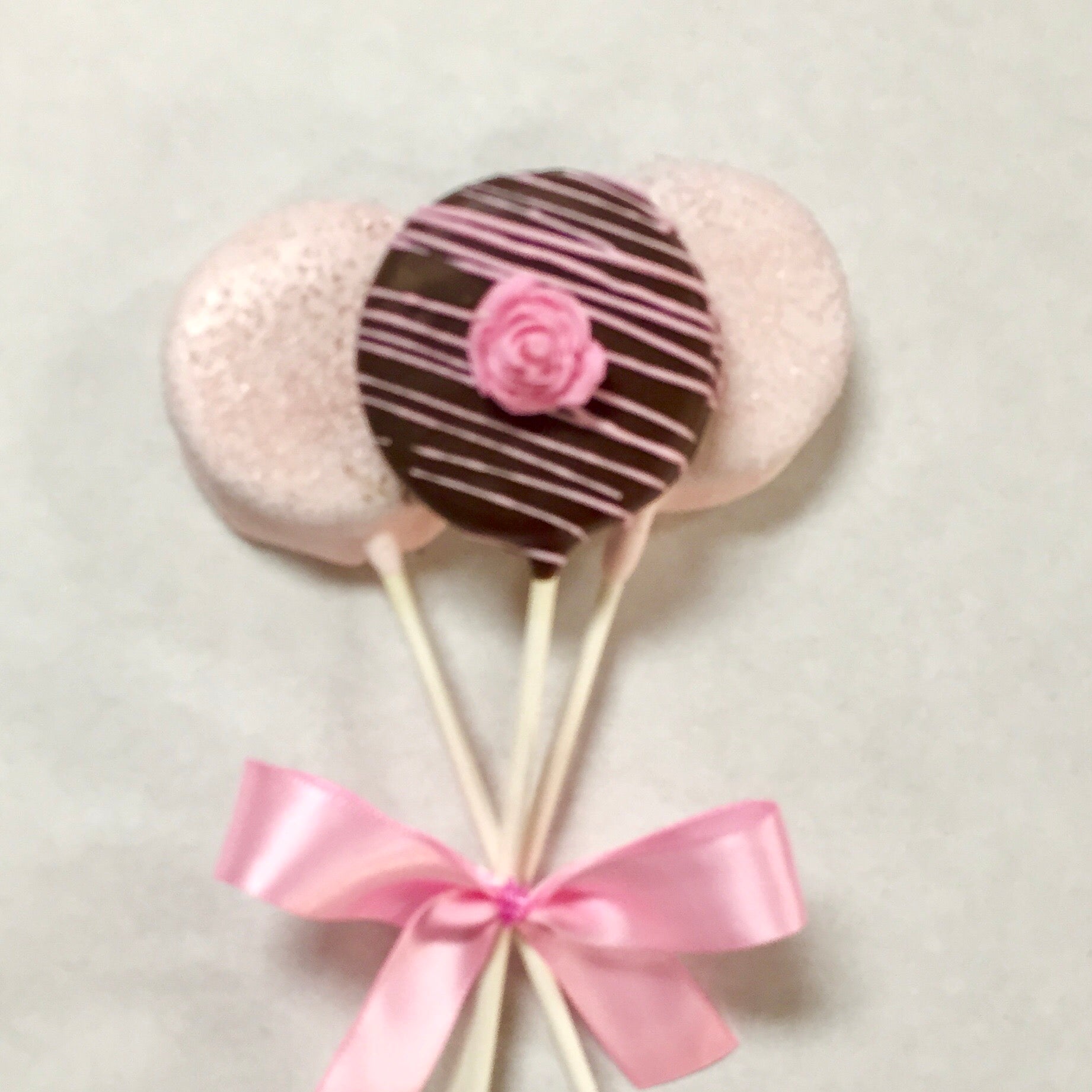 Chocolate covered Oreo with light pink drizzle and chocolate rose and 2 light pink covered Oreos with sanding sugar wrapped as a trio