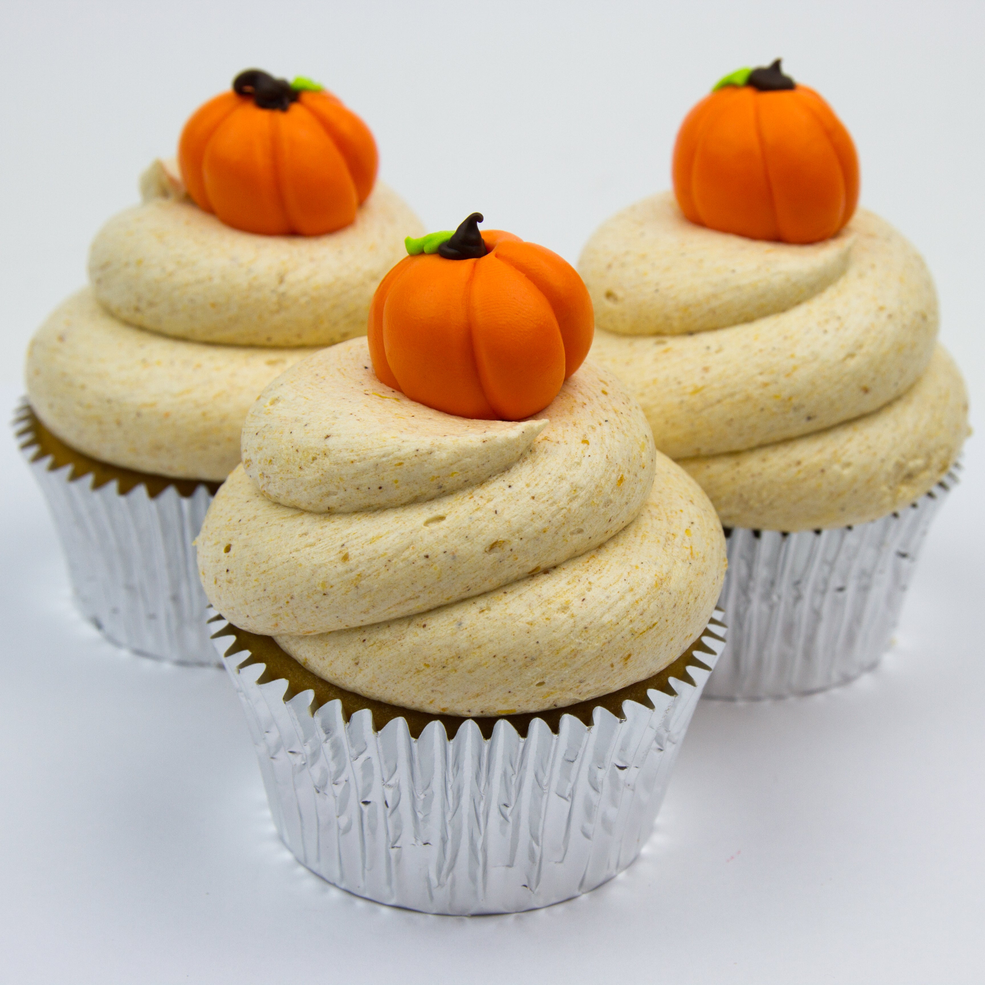 Pumpkin flavored cupcake iced with pumpkin flavored buttercream and topped with a handmade fondant pumpkin design can vary