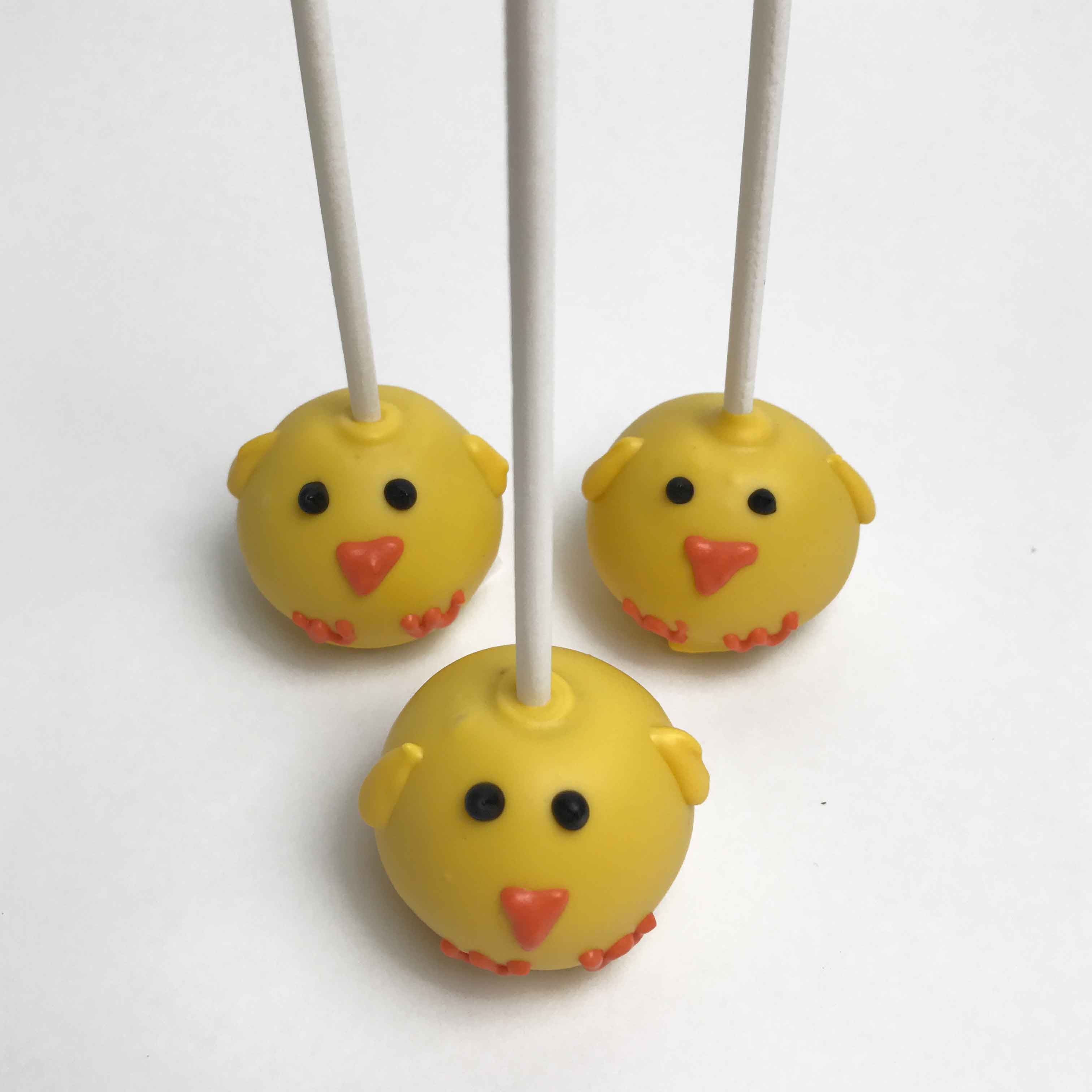 Three yellow Easter Chick Cake Pops with black eyes and orange beaks and feet