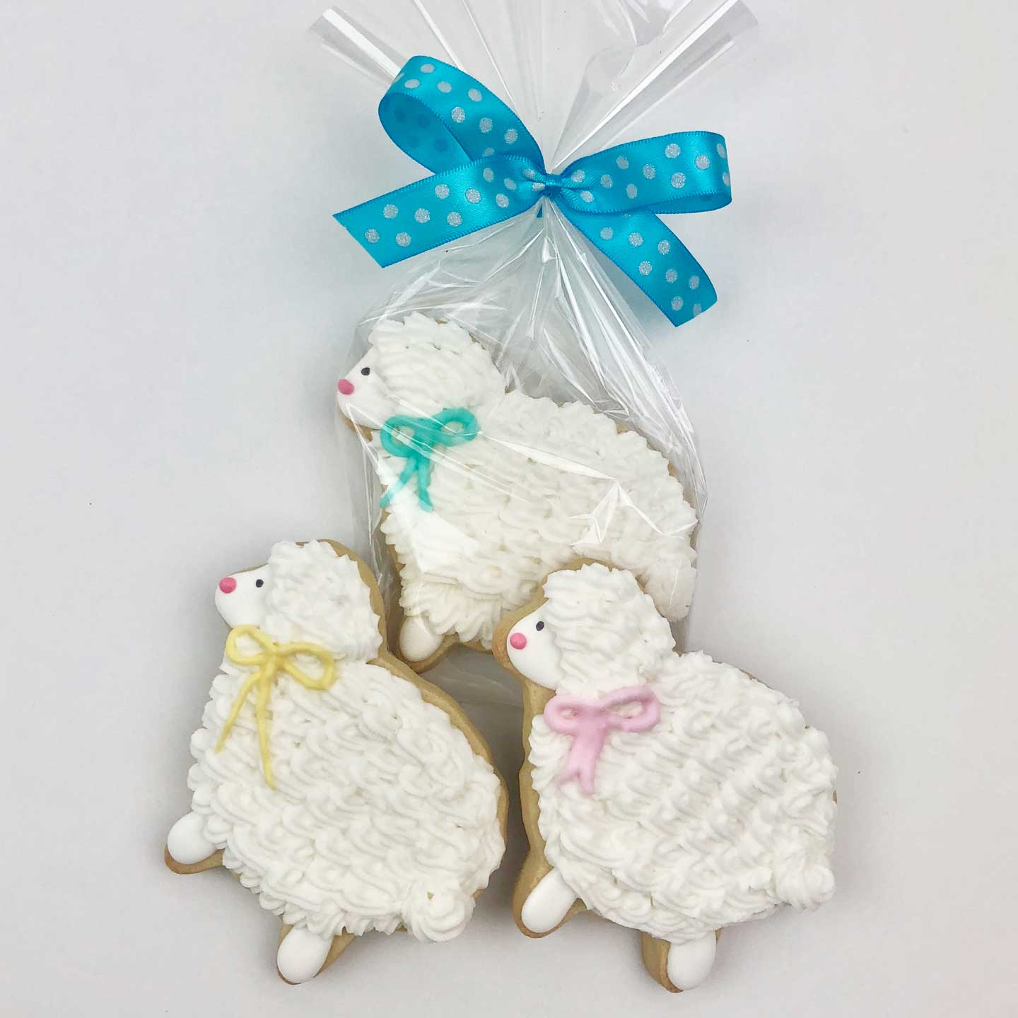 Three white color lamb Cookies, one warped in cellophane with a blue ribbon with white polk dots