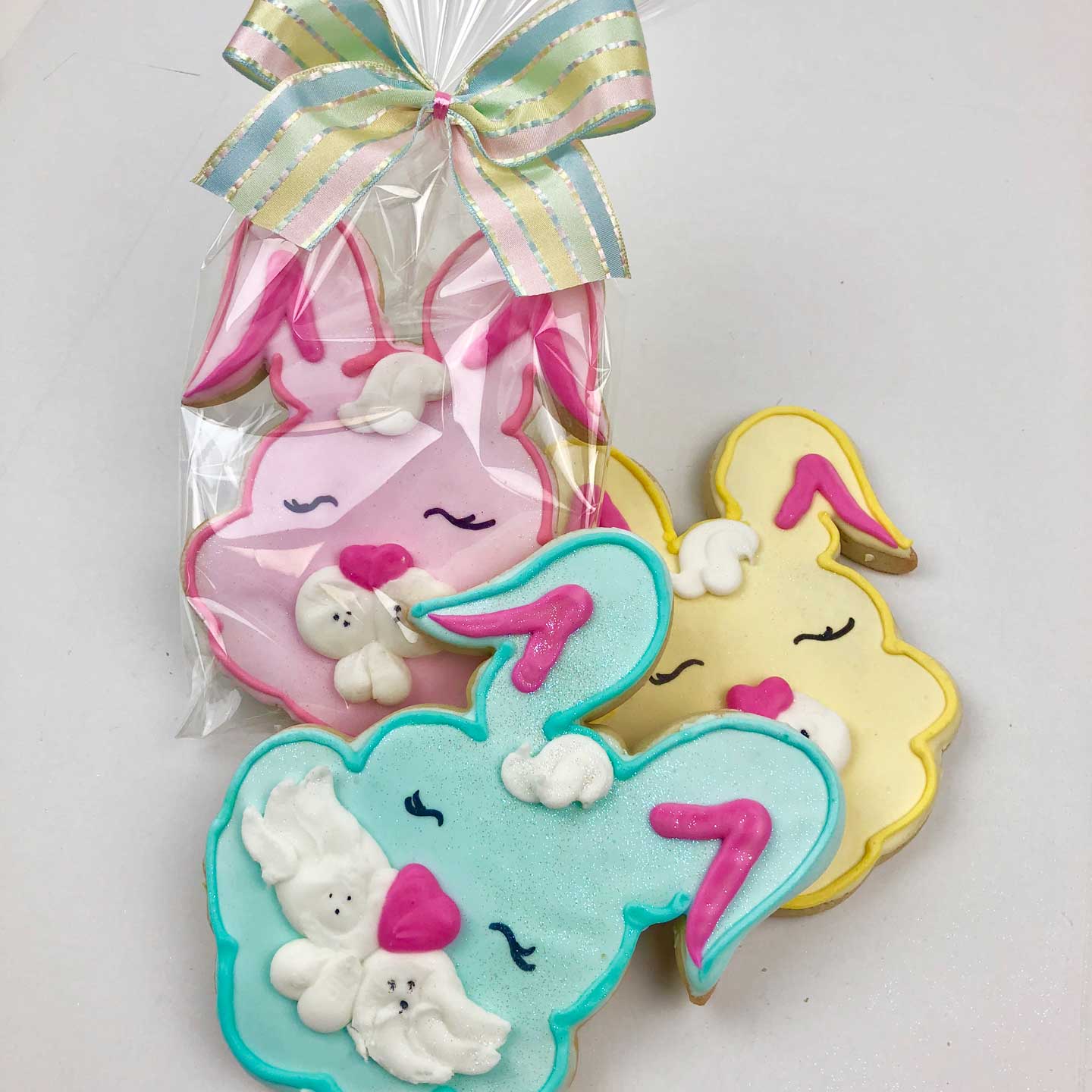 Three pink, blue, and yellow bunny face Cookies. The Pink one is warped in cellophane with a ribbon