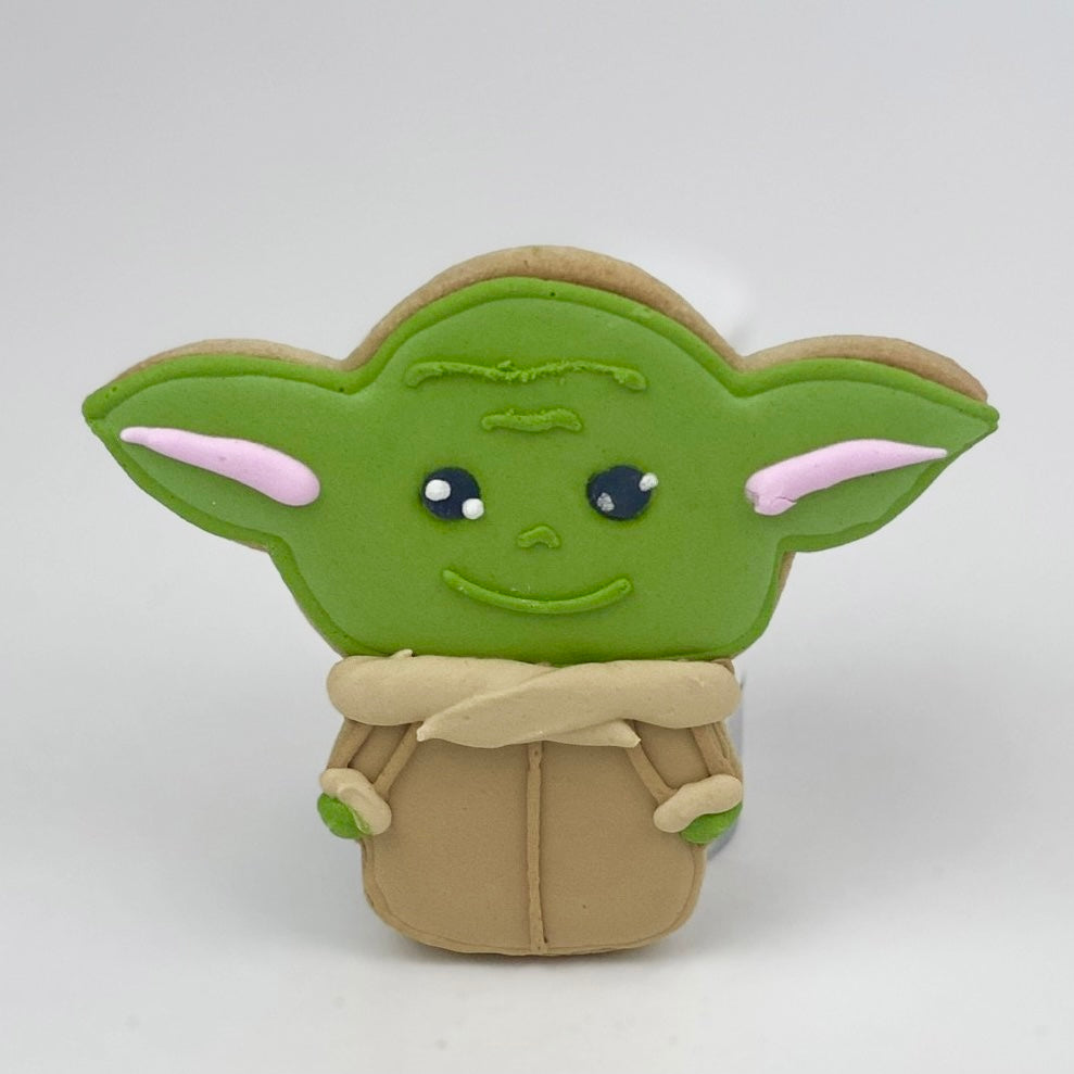 The green Child shortbread cookie, dressed in a beige coat.