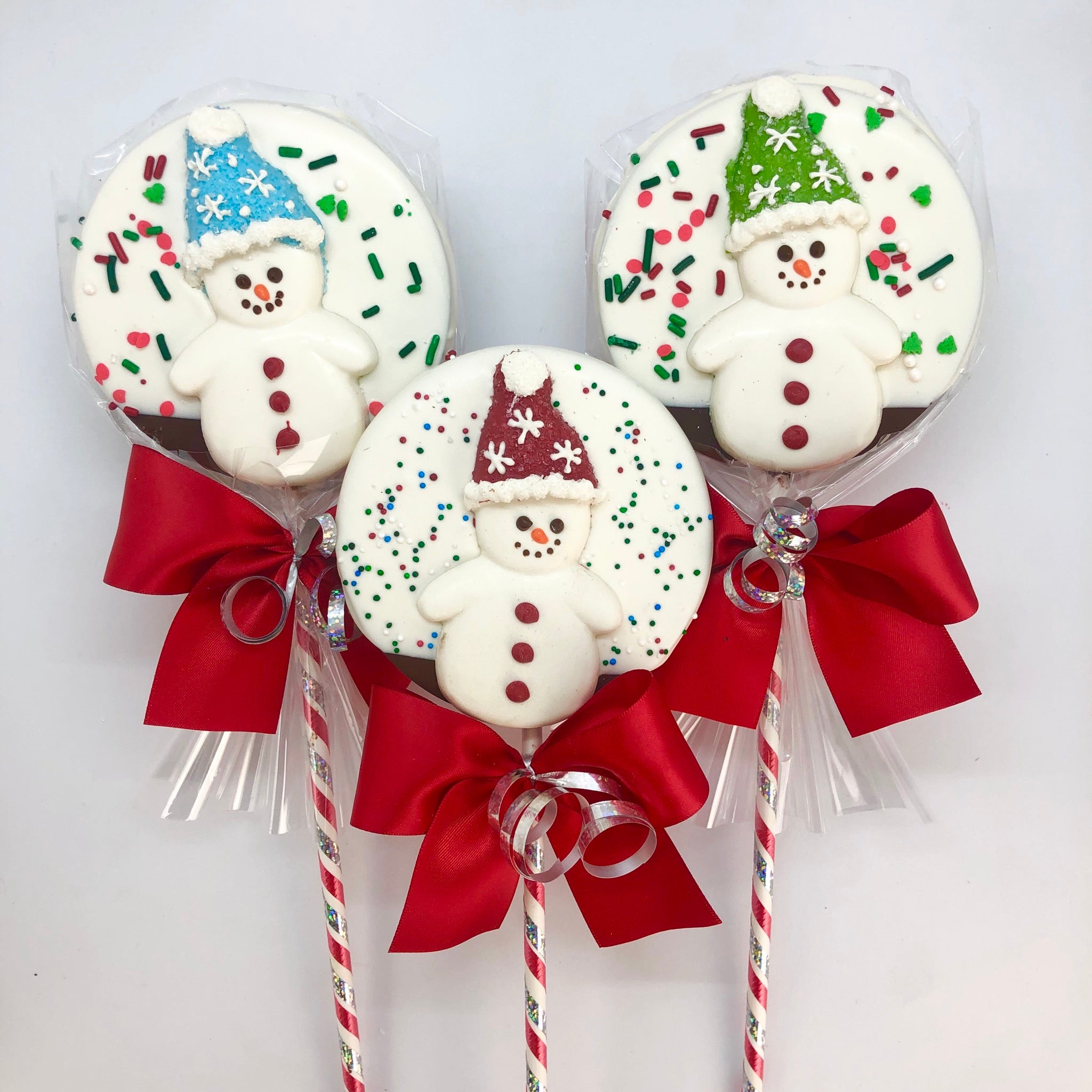 Snowman Chocolate Crispy Lollies, wearing blue, red, and green hats and wrapped in cellophane with a ribbon