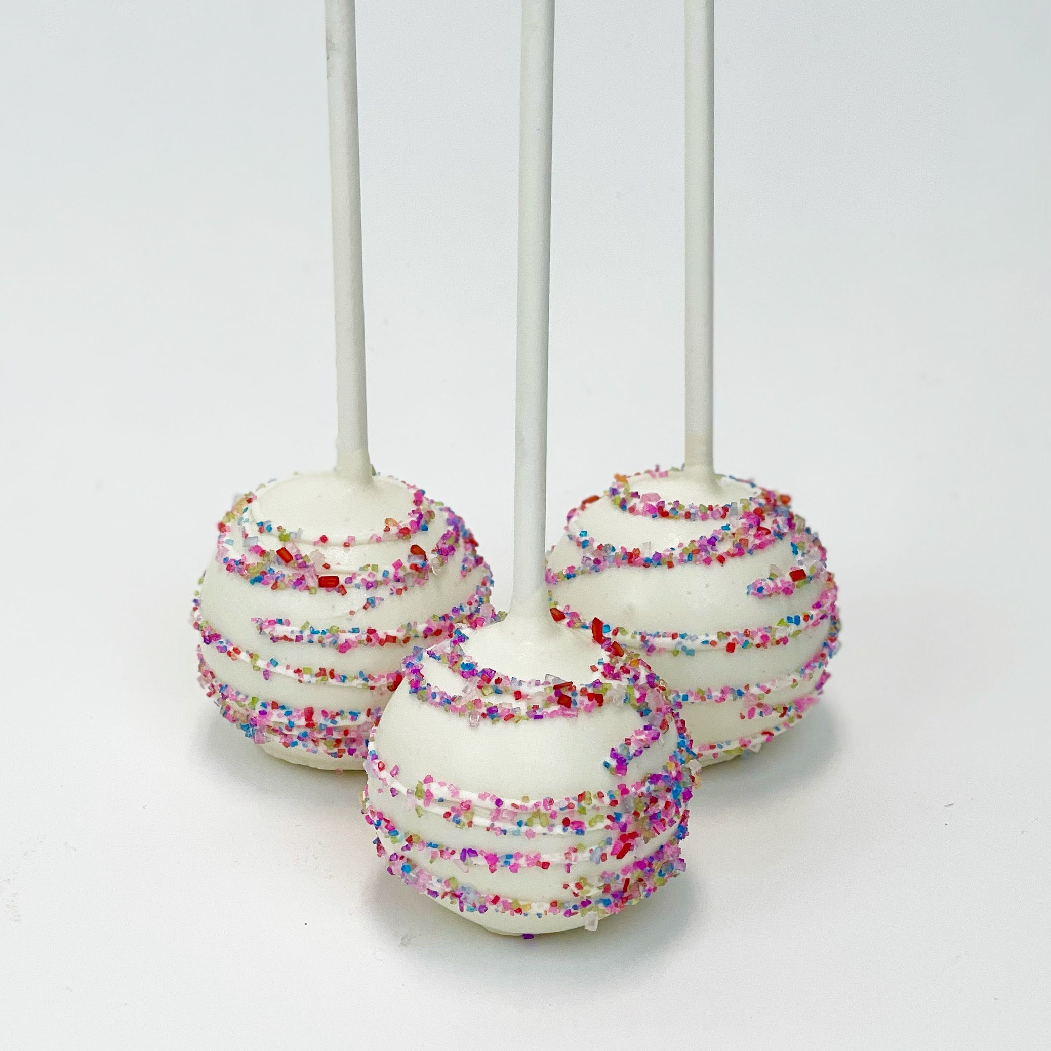 Three white cake pops decorated with a multi-colored swirl of sanding sugar