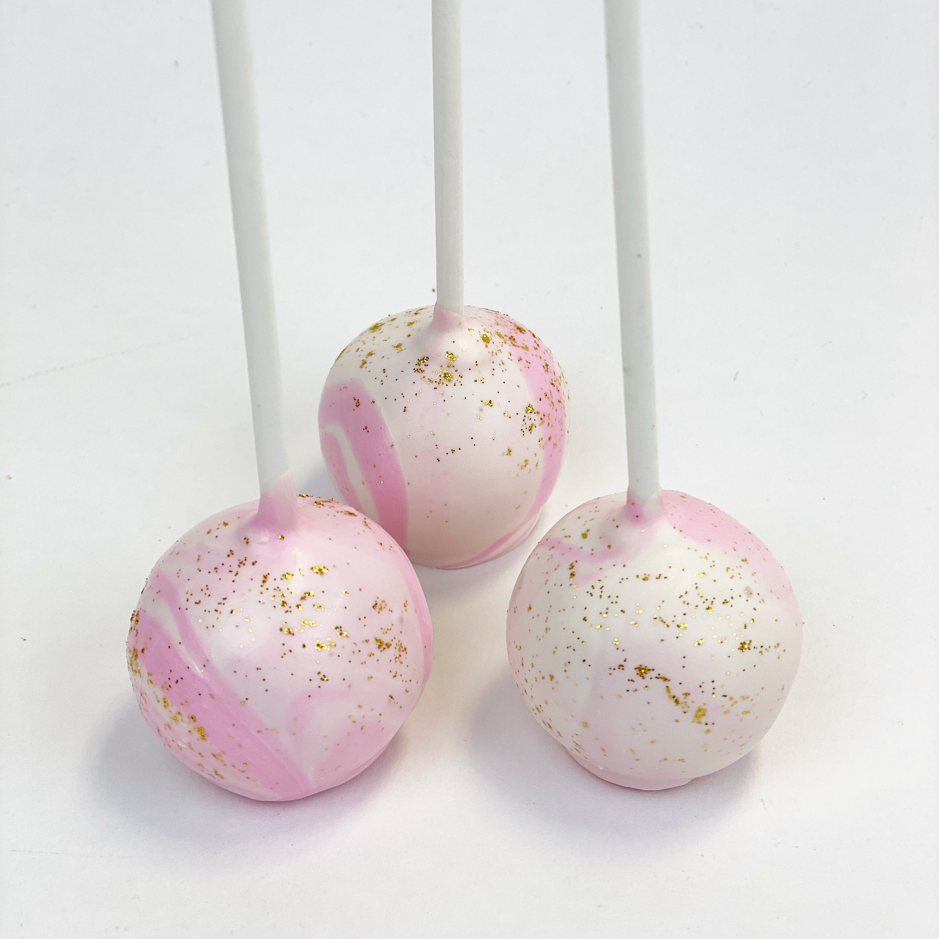 Three cake pops with a pink and white marbled dip and gold dust