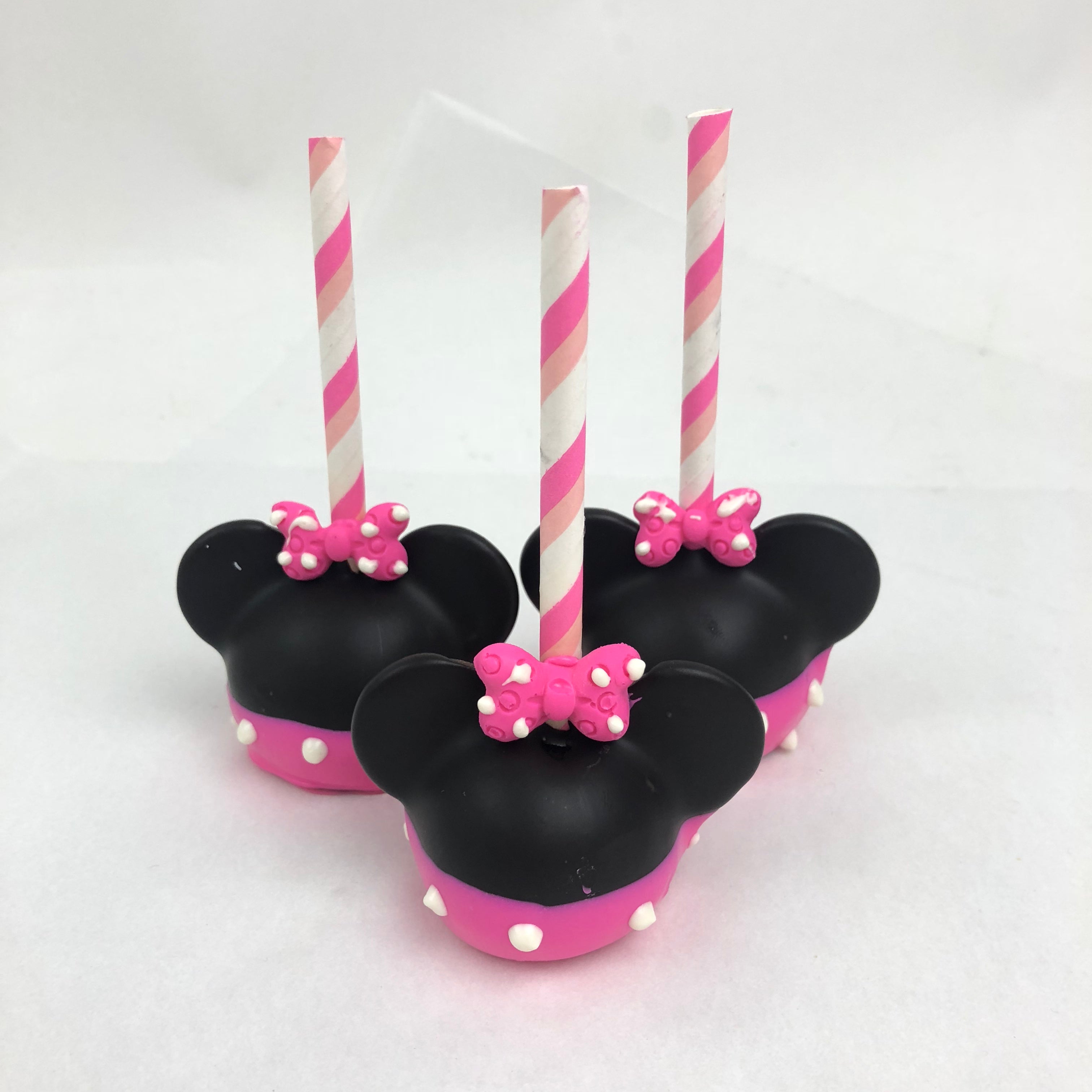 Three mini mouse cake pops with pink bottoms and white polka dots, black Mini Mouse hats, and pink bows with white polka dots