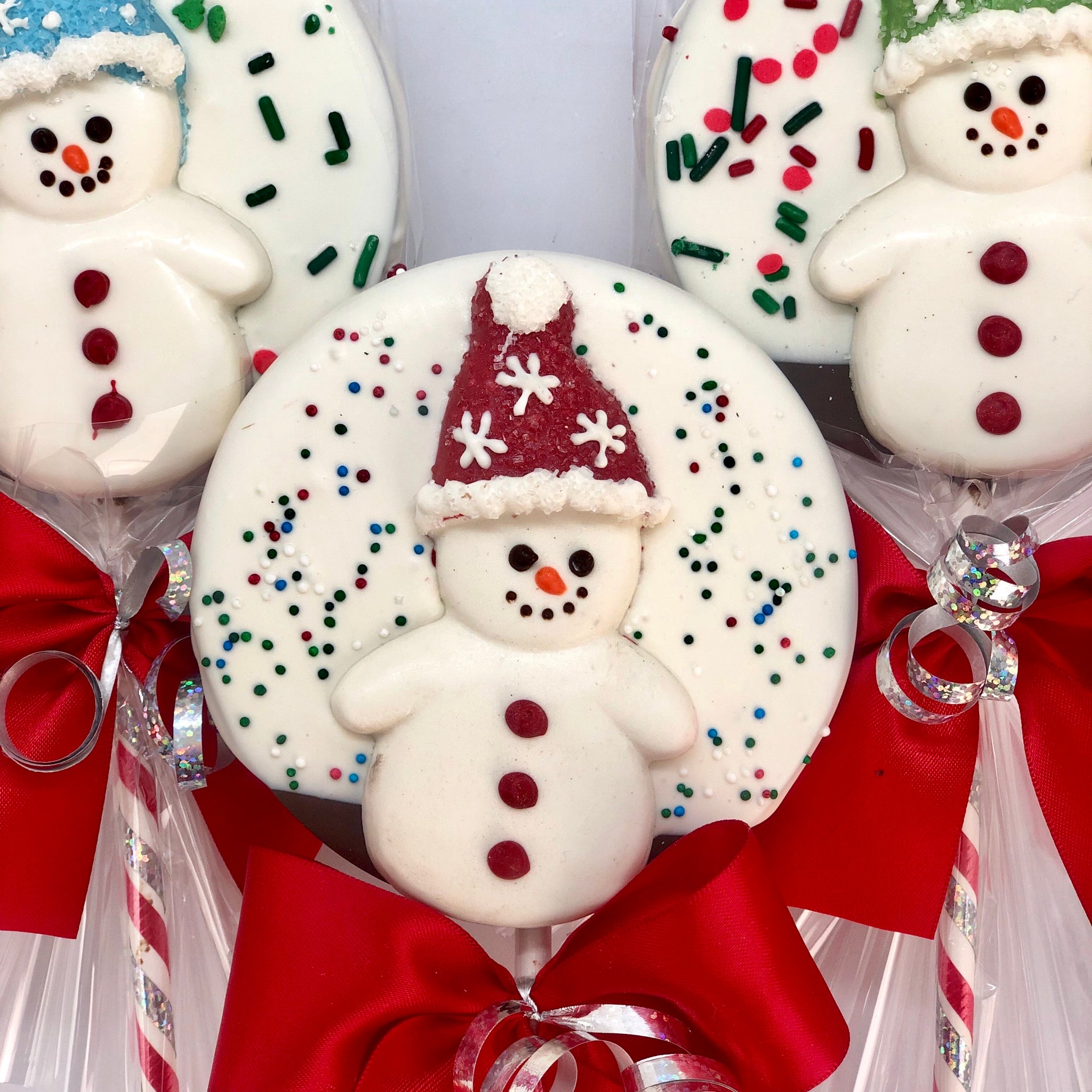 Snowman Chocolate Crispy Lollies, wearing blue, red, and green hats and wrapped in cellophane with a ribbon