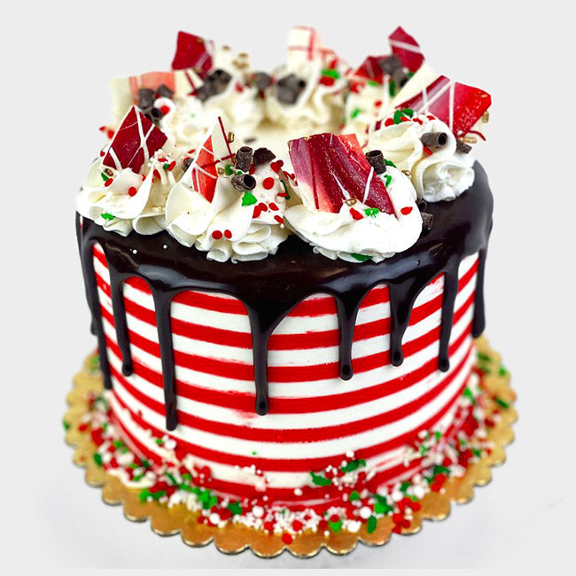 A red and white striped cake with a chocolate ganache drip adorned with chocolate pieces and buttercream dollops.
