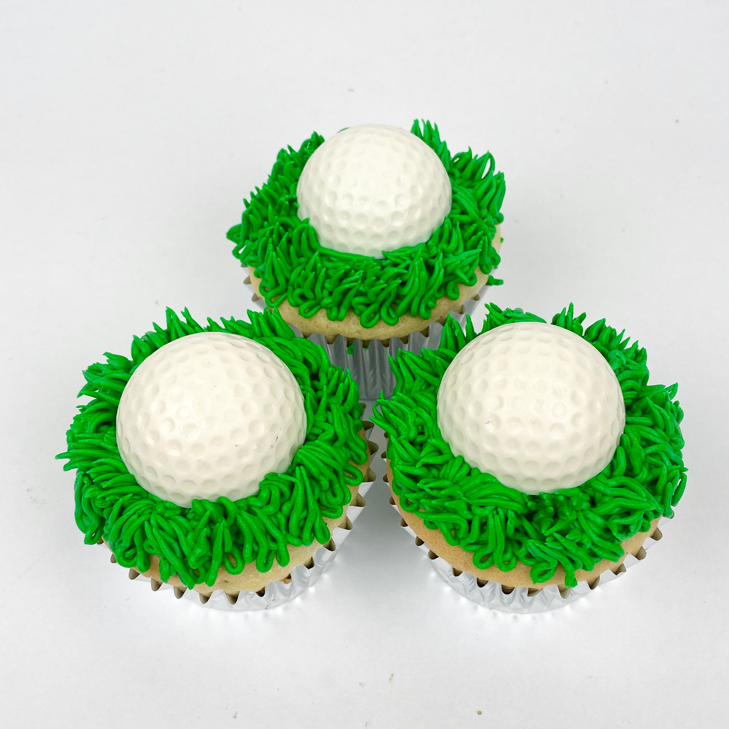 Three cupcakes iced in grass green buttercream and topped with a white chocolate golf ball.