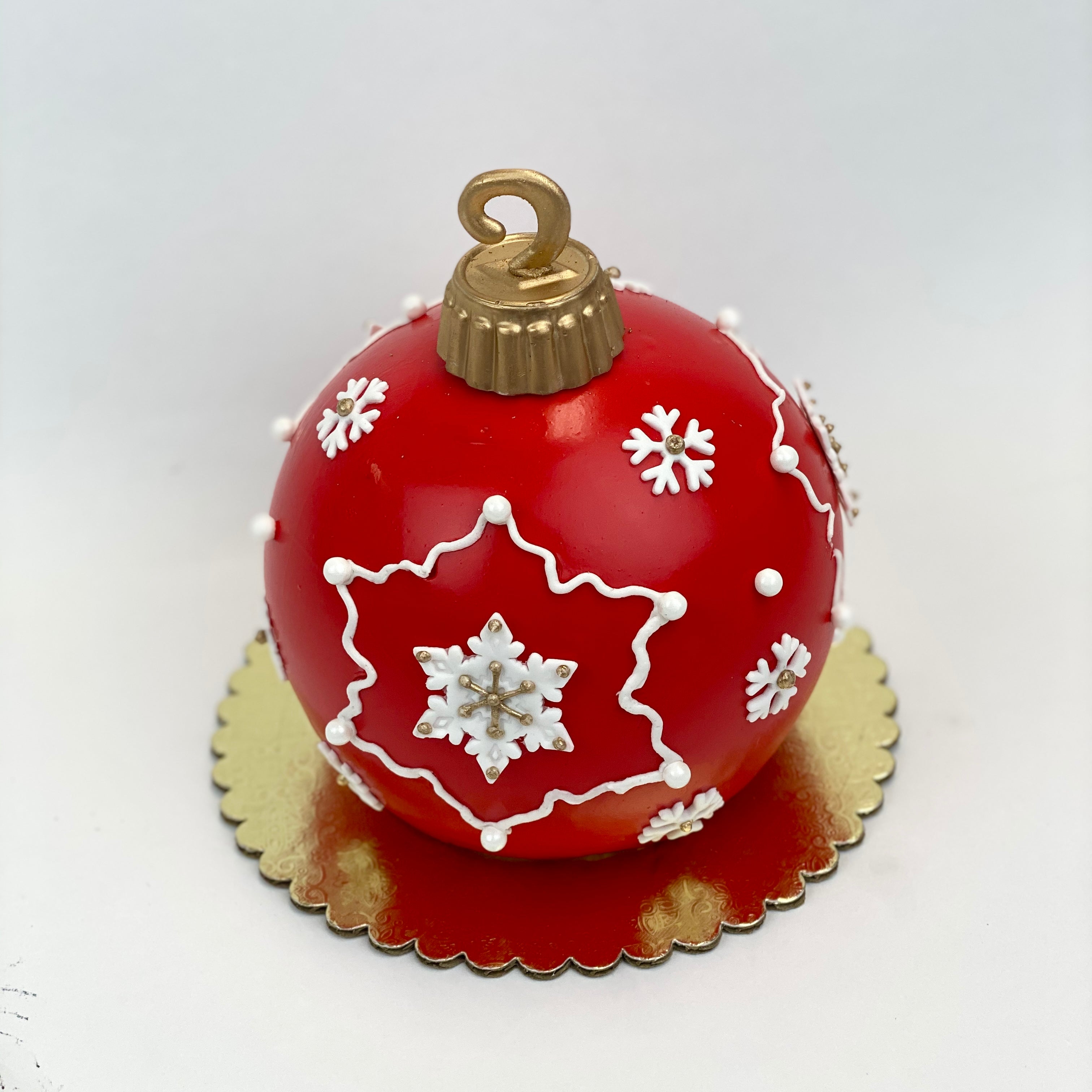 A round ornament ball cake covered with red fondant and decorated with white snowflakes.