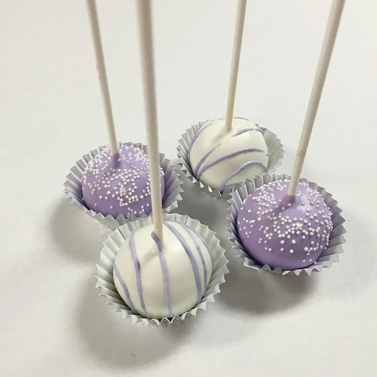 Two lavender cake pops decorated with white nonpareils. Two white cake pops decorated with lavender chocolate drizzle