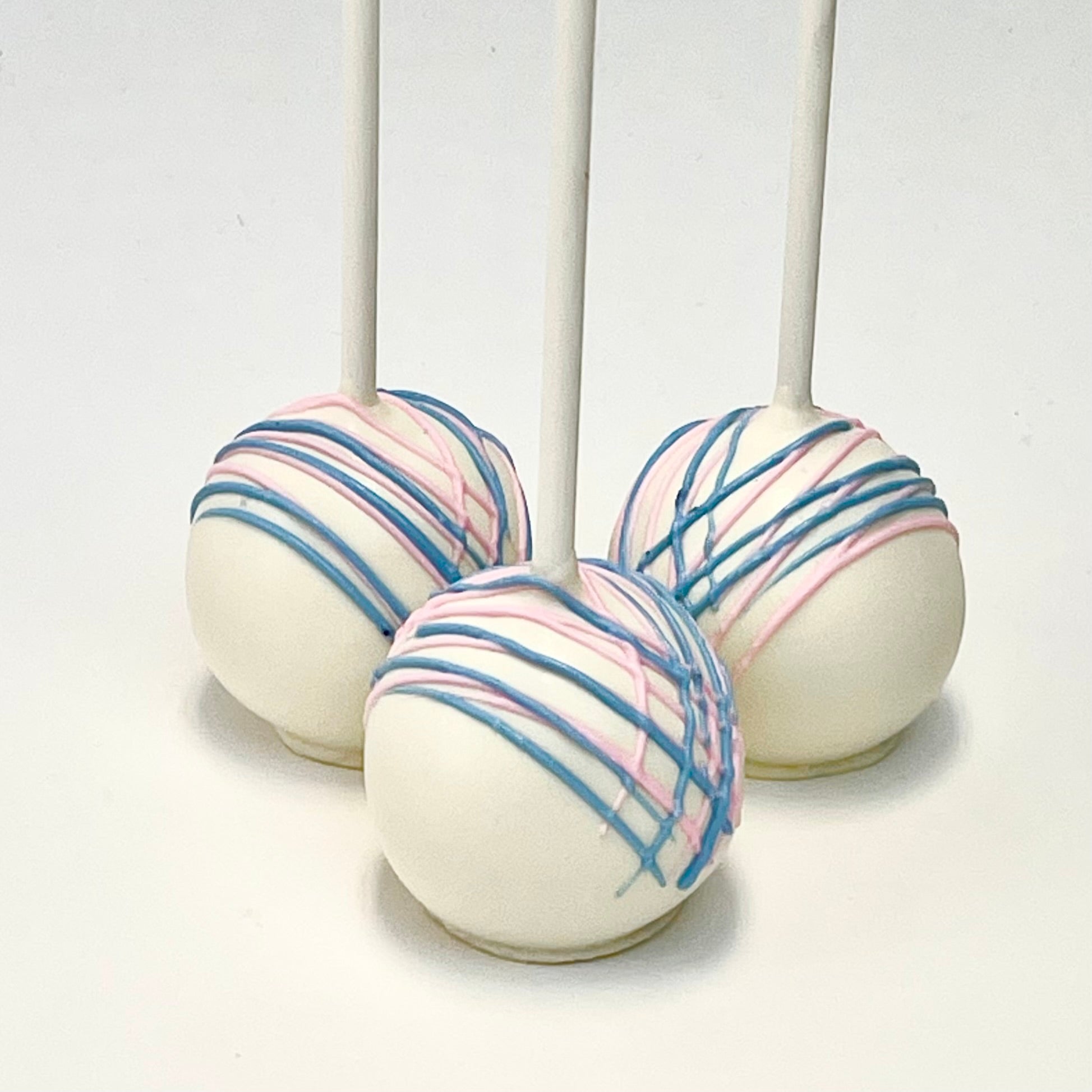 Three white cake pops with a light pink and light blue drizzles