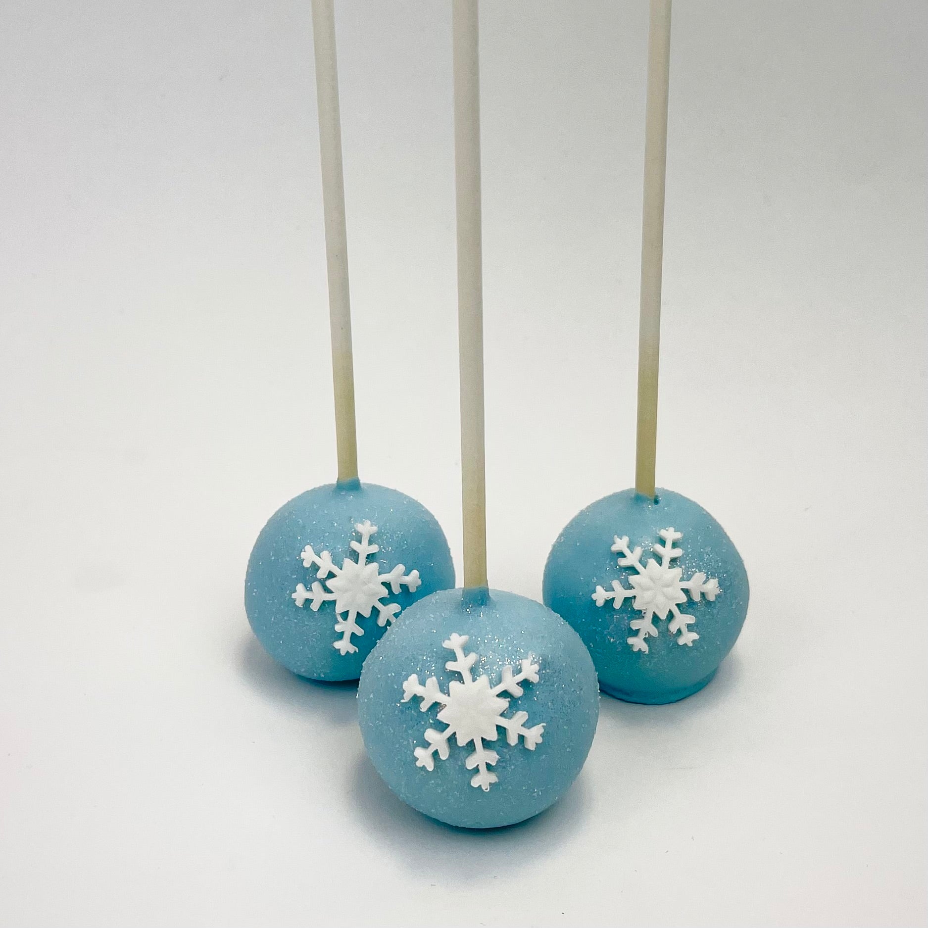 Three blue Cake Pops decorated with a white fondant snowflake