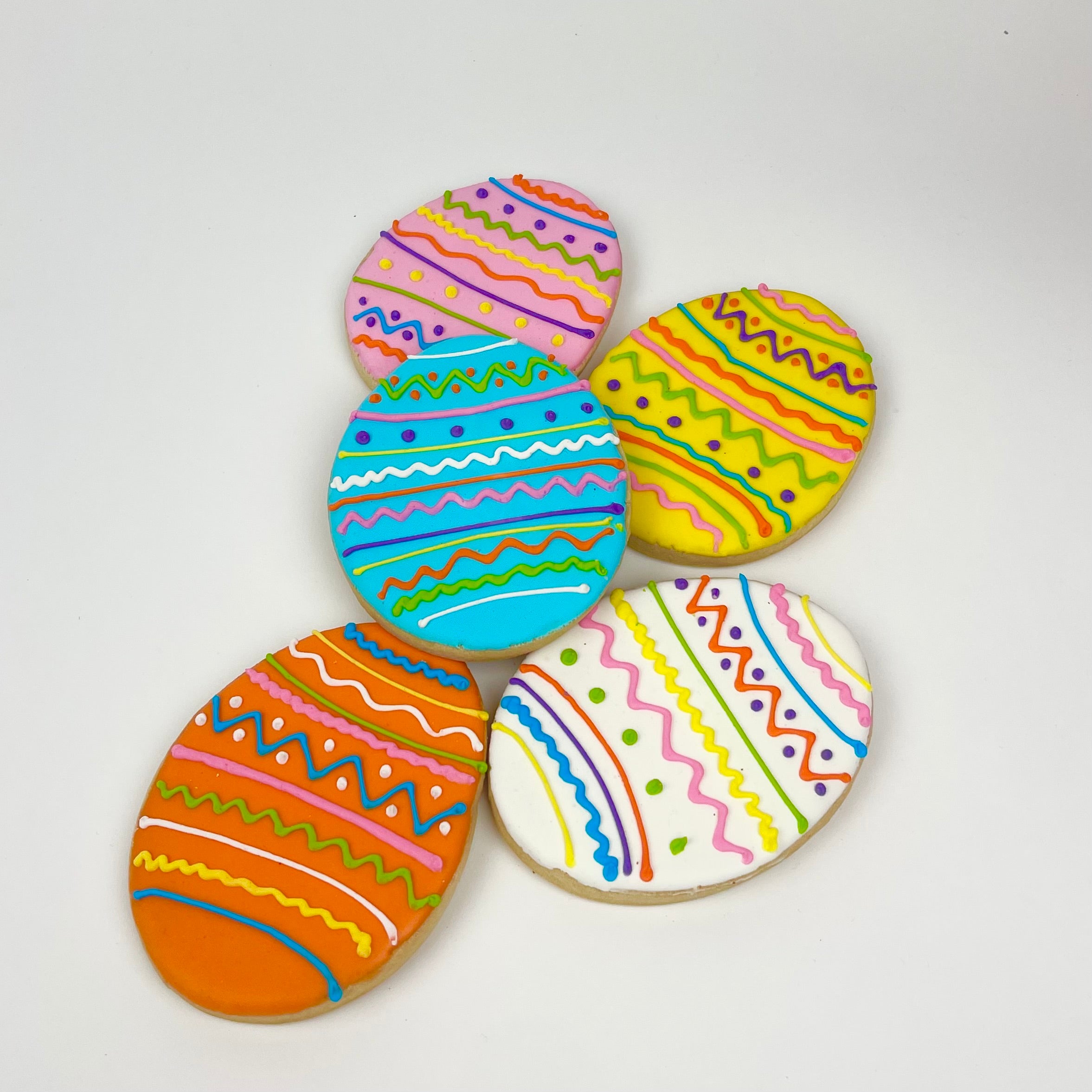 Five decorated pink, yellow, blue, white, and orange sugar cookies