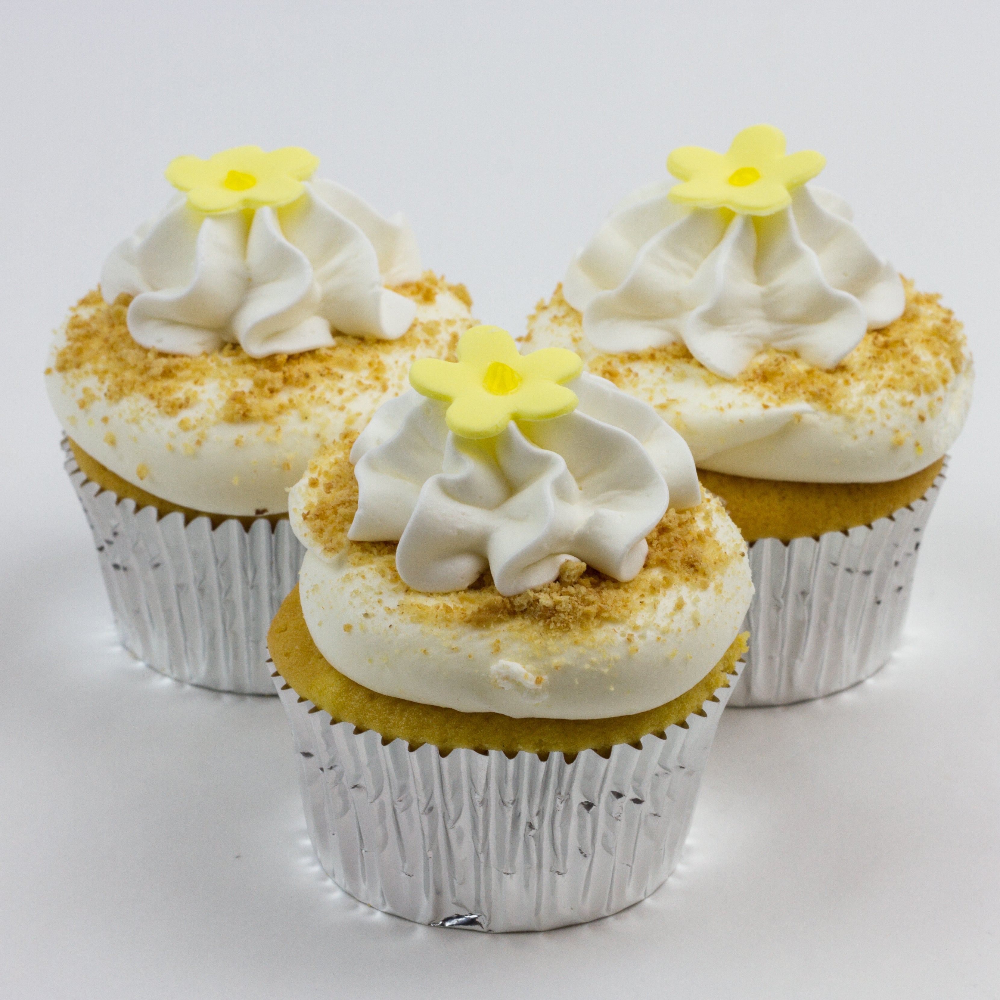 Three lemon cupcakes topped with a lightly flavored lemon buttercream, white buttercream swirl, graham crackers and a yellow fondant flower with edible glitter