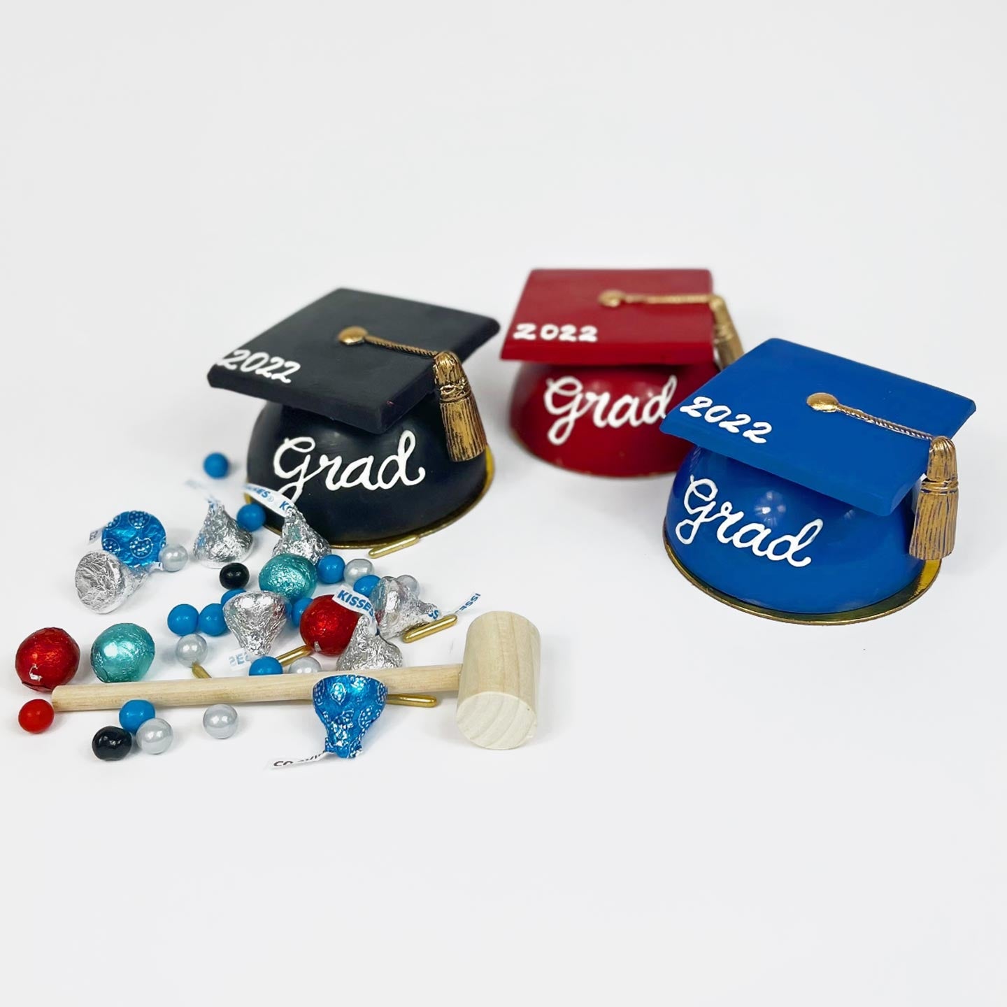 Three chocolate graduation caps in black, red, and blue. Each graduation cap includes assorted candies on the inside. The assorted candy and a mallot are shown on the outside.