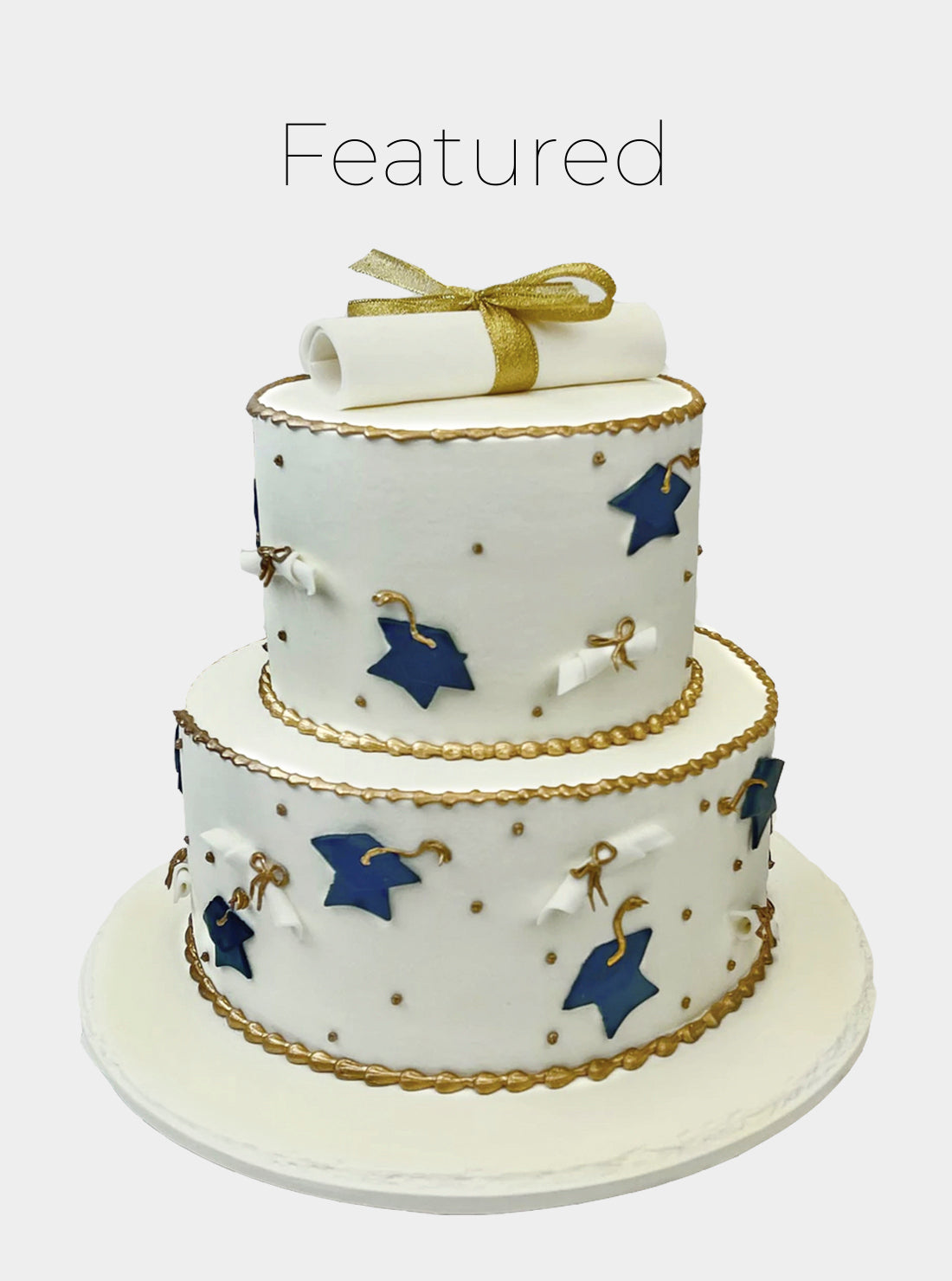 Two tier graduation cake with graduation hats and diplomas all over the cake with a diploma on top