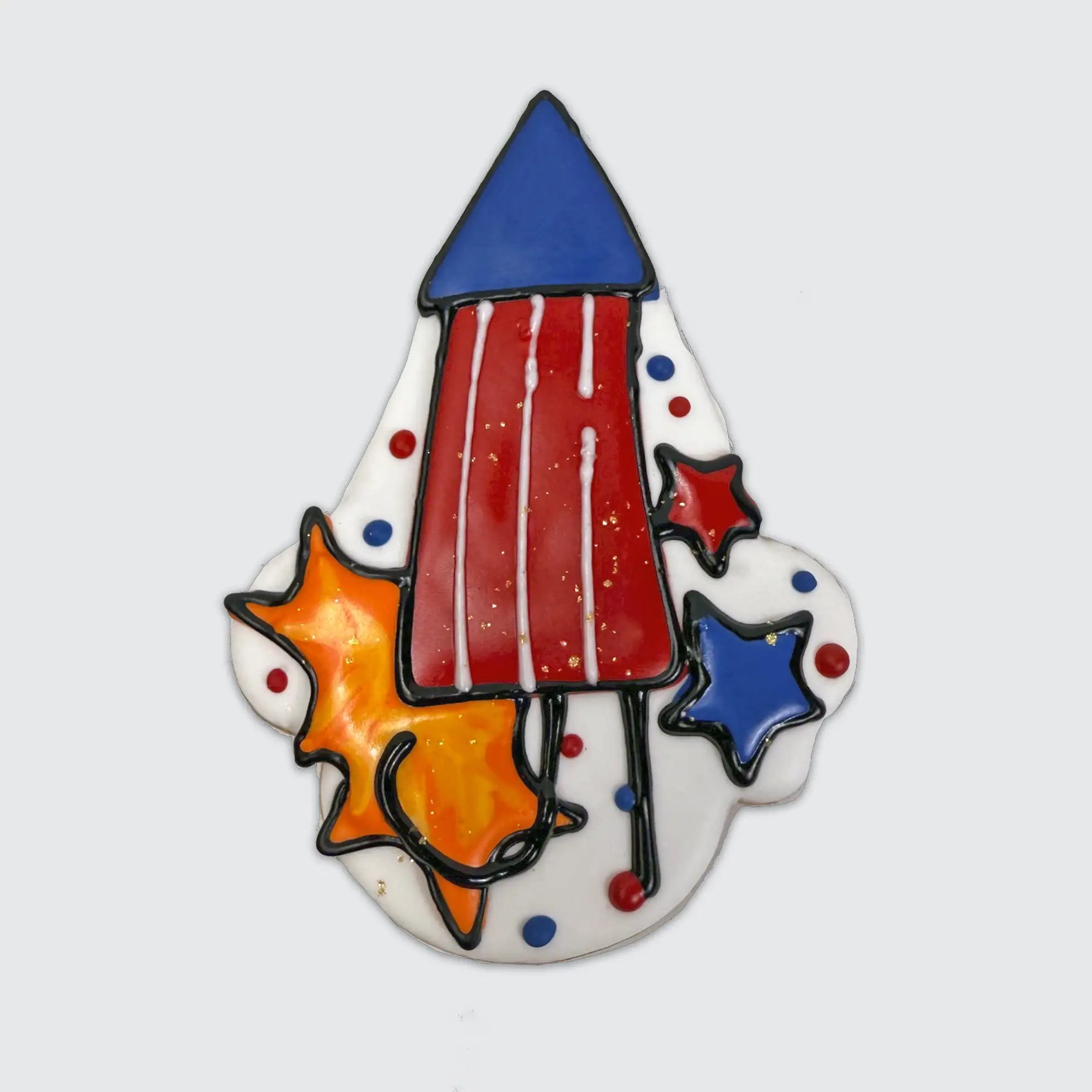A festive 4th of July sugar cookie, featuring a red rocket, blue cone top, surrounded by red and blue stars and orange color bursts of icing designed to resemble fireworks.