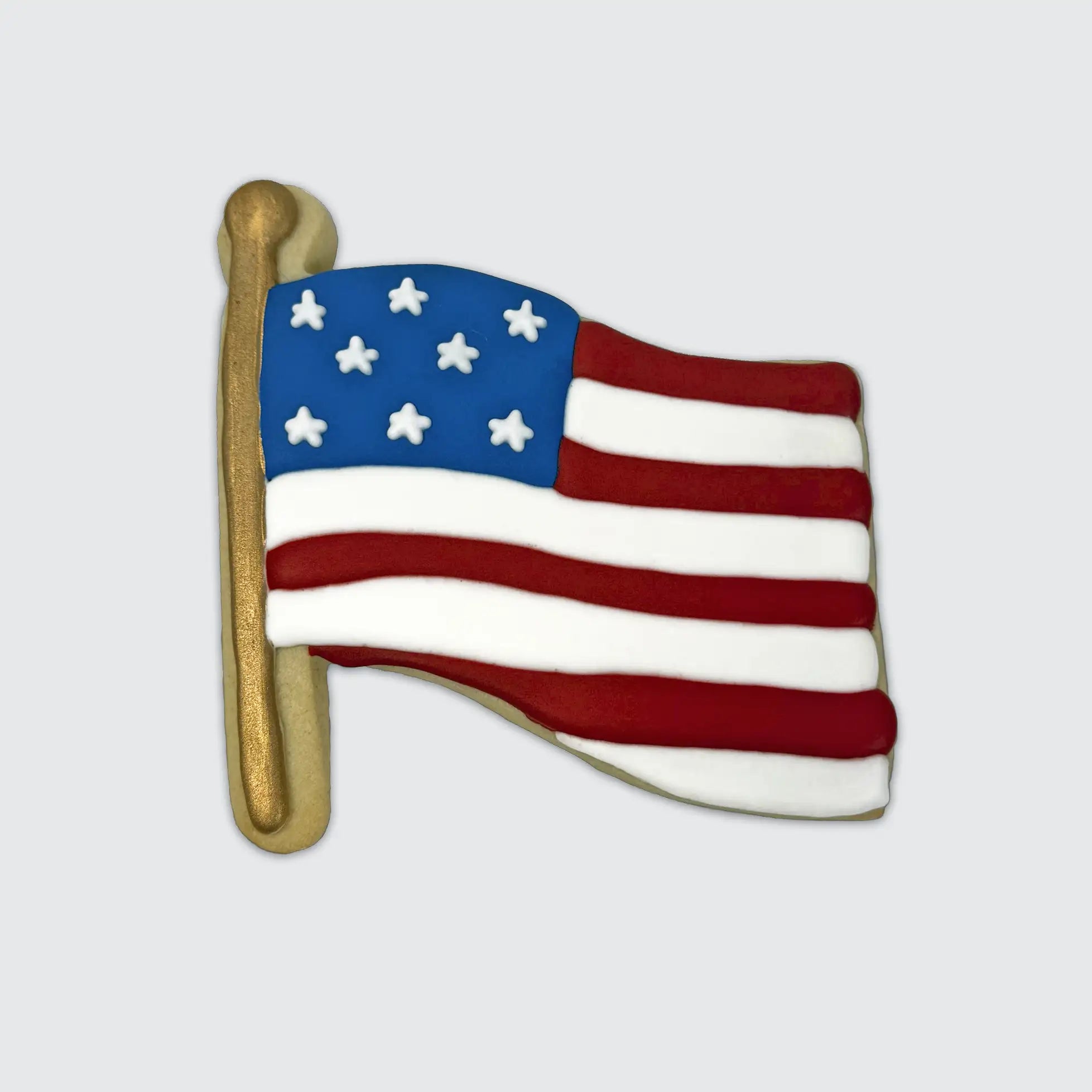 American flag-shaped sugar cookie with red and white stripes, blue star field, and gold flagpole.