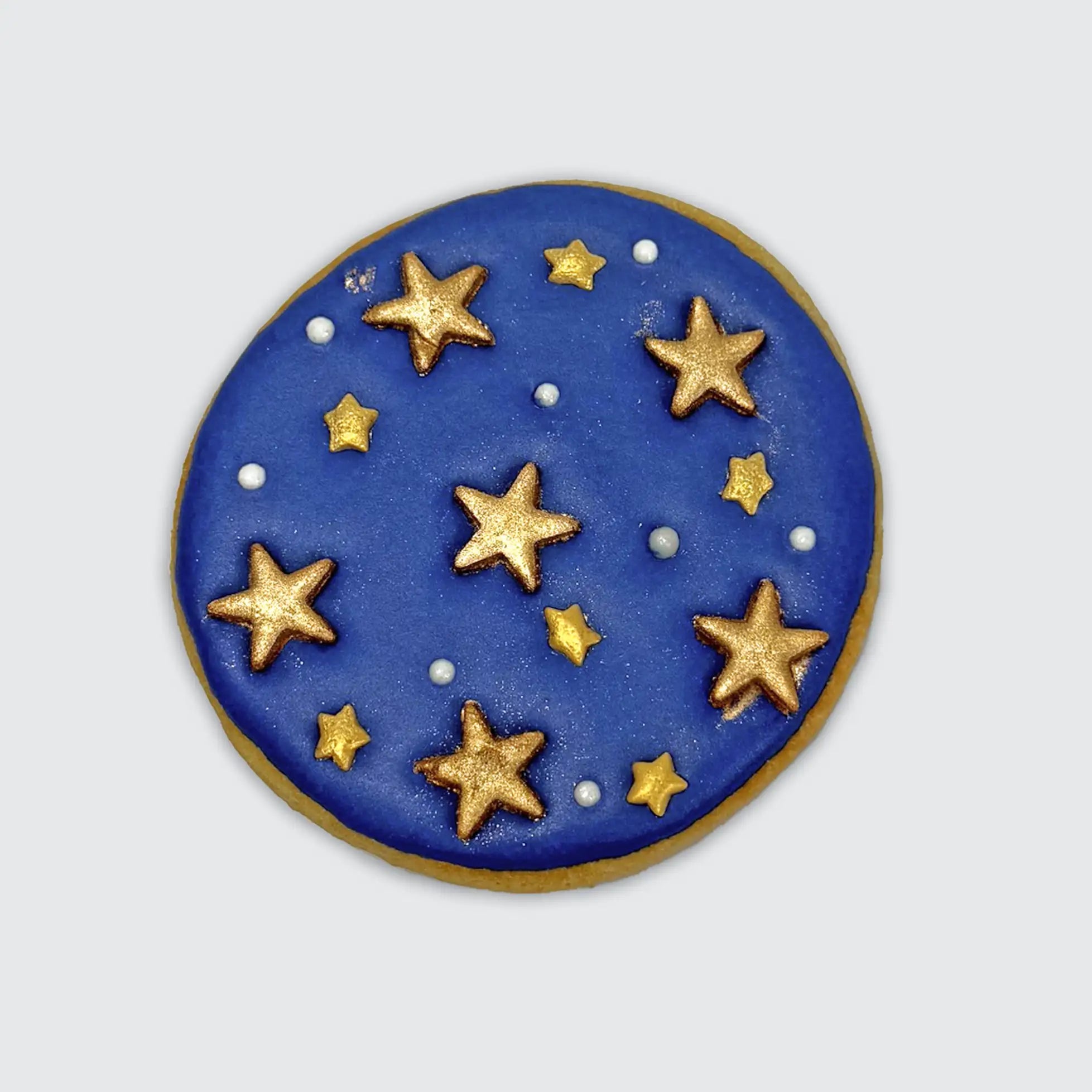 Round sugar cookie with blue icing decorated with gold stars and silver pearl-like dots resembling a night sky.