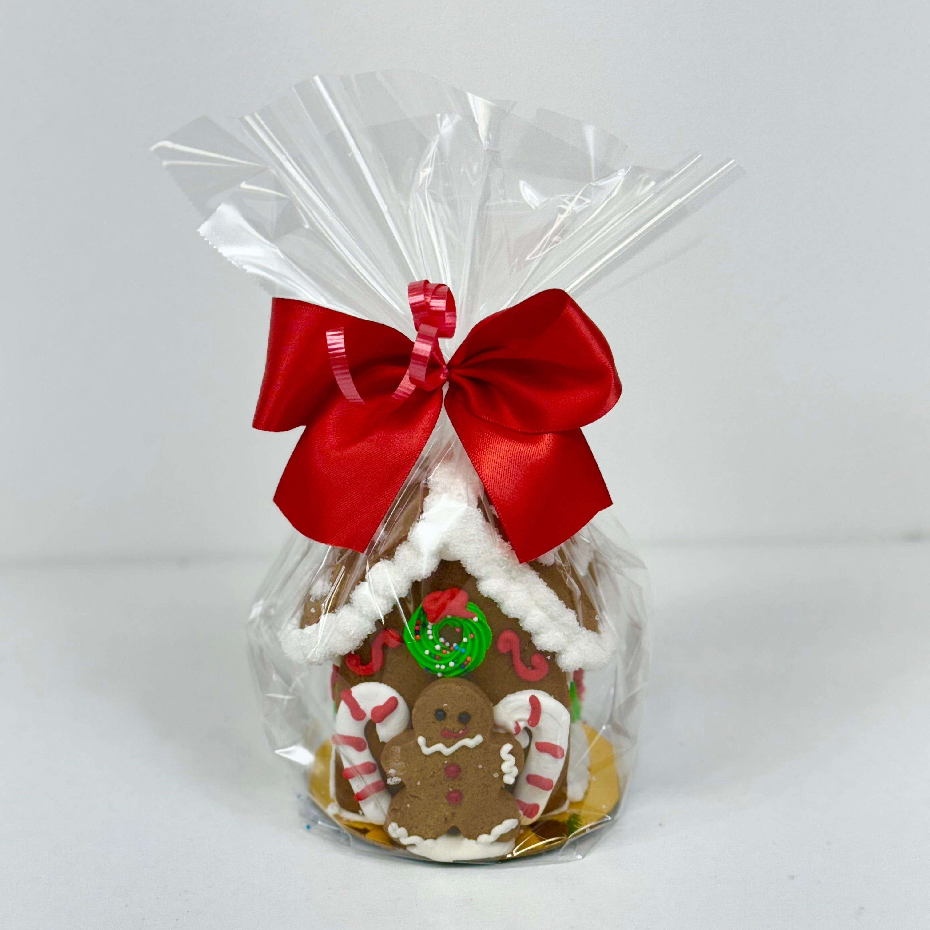 A mini gingerbread house on a 4" round gold board, wrapped in cello and tie with a satin bow.