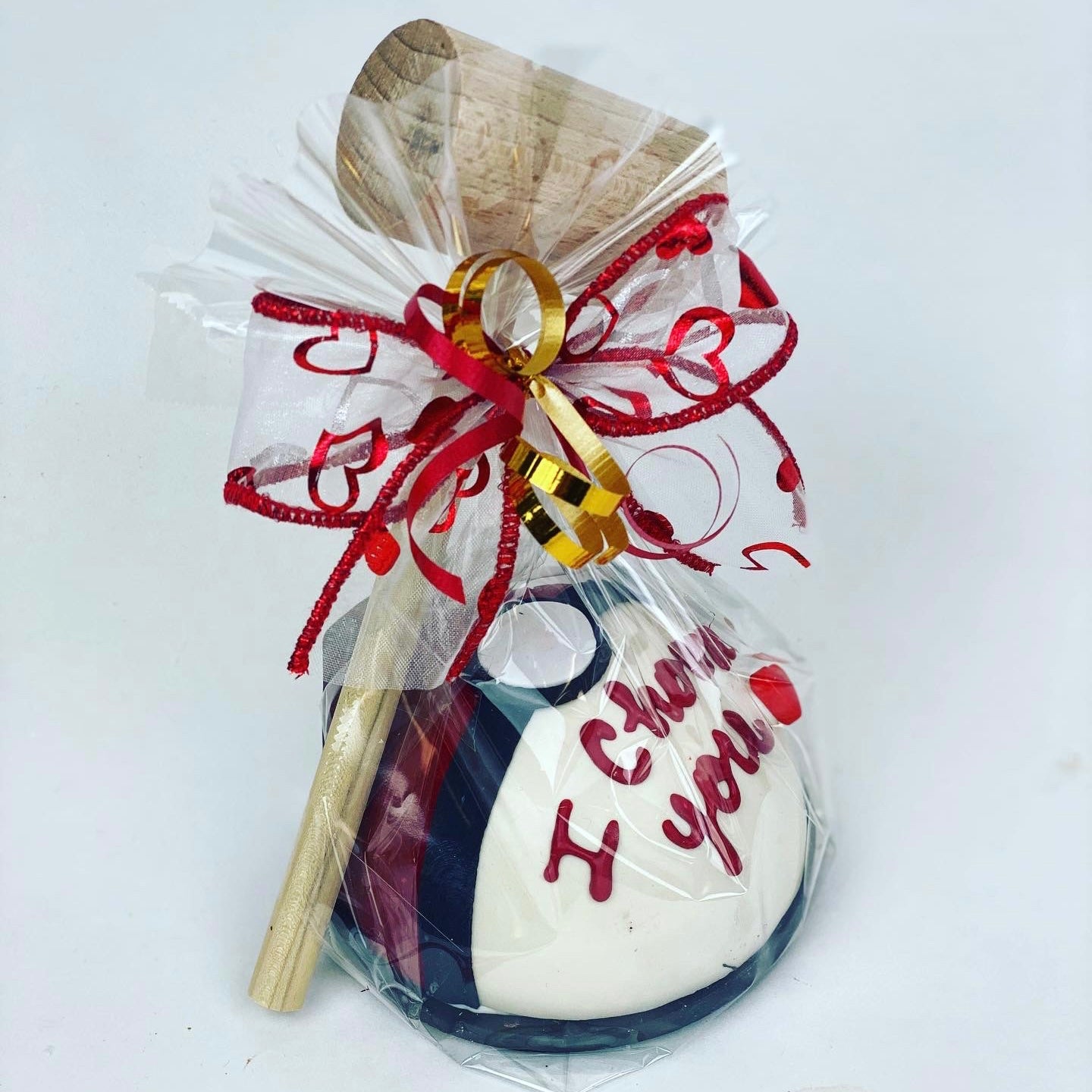 A white, red, and black 4” candy-filled chocolate piñata with the saying ""I Choose You" written on it. It is wrapped in clear cellophane with a wooden mallet and red and gold ribbons.