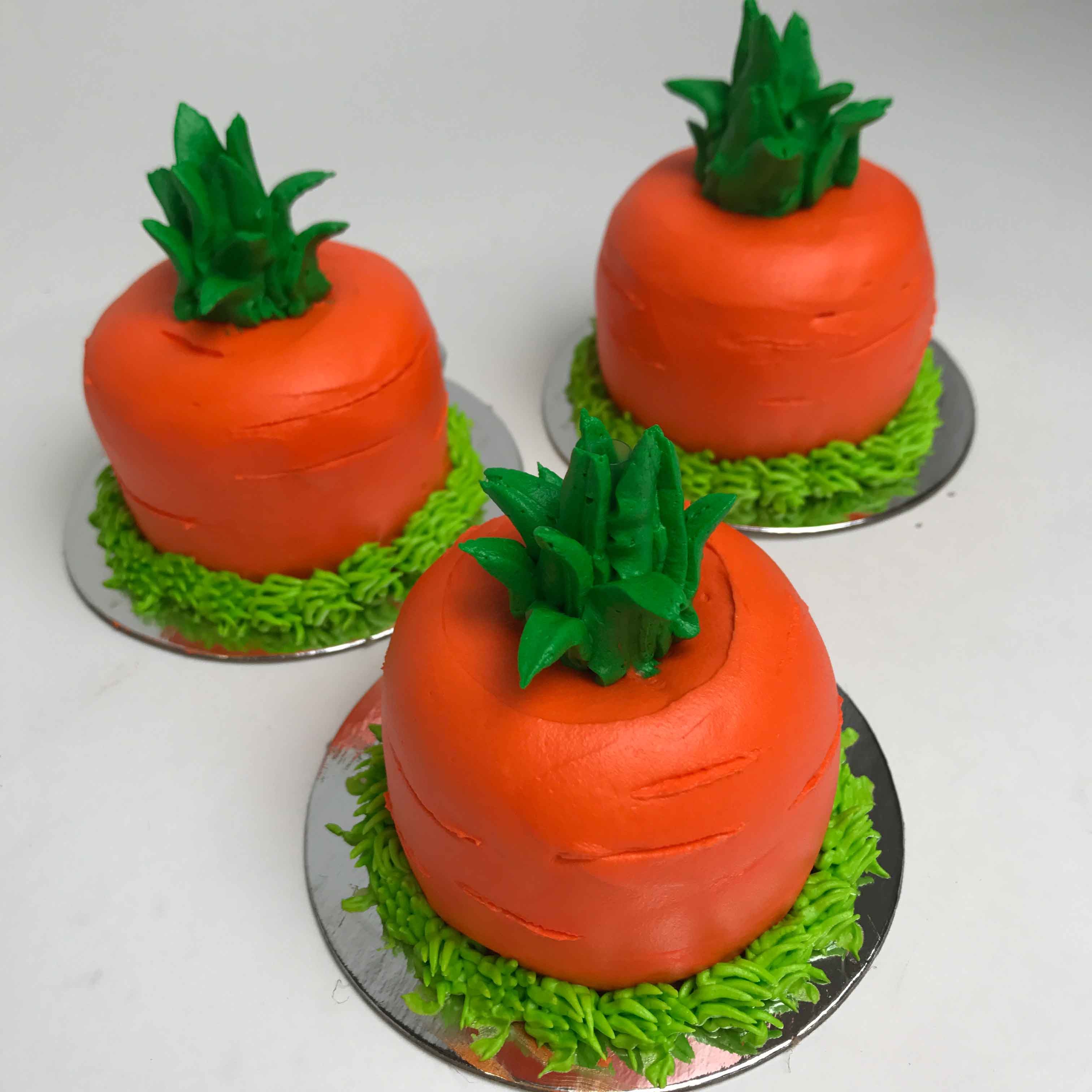 Three orange Easter Carrot 3D Cupcakes sitting individually on a silver base.