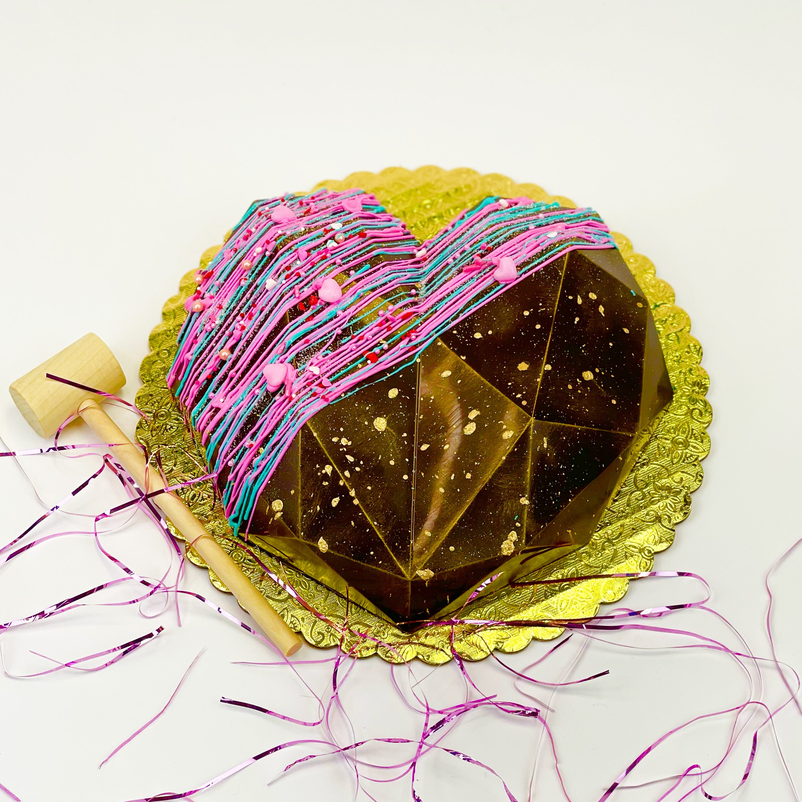 Candy-filled Chocolate geode heart next to a wooden mallet on a 9" board.