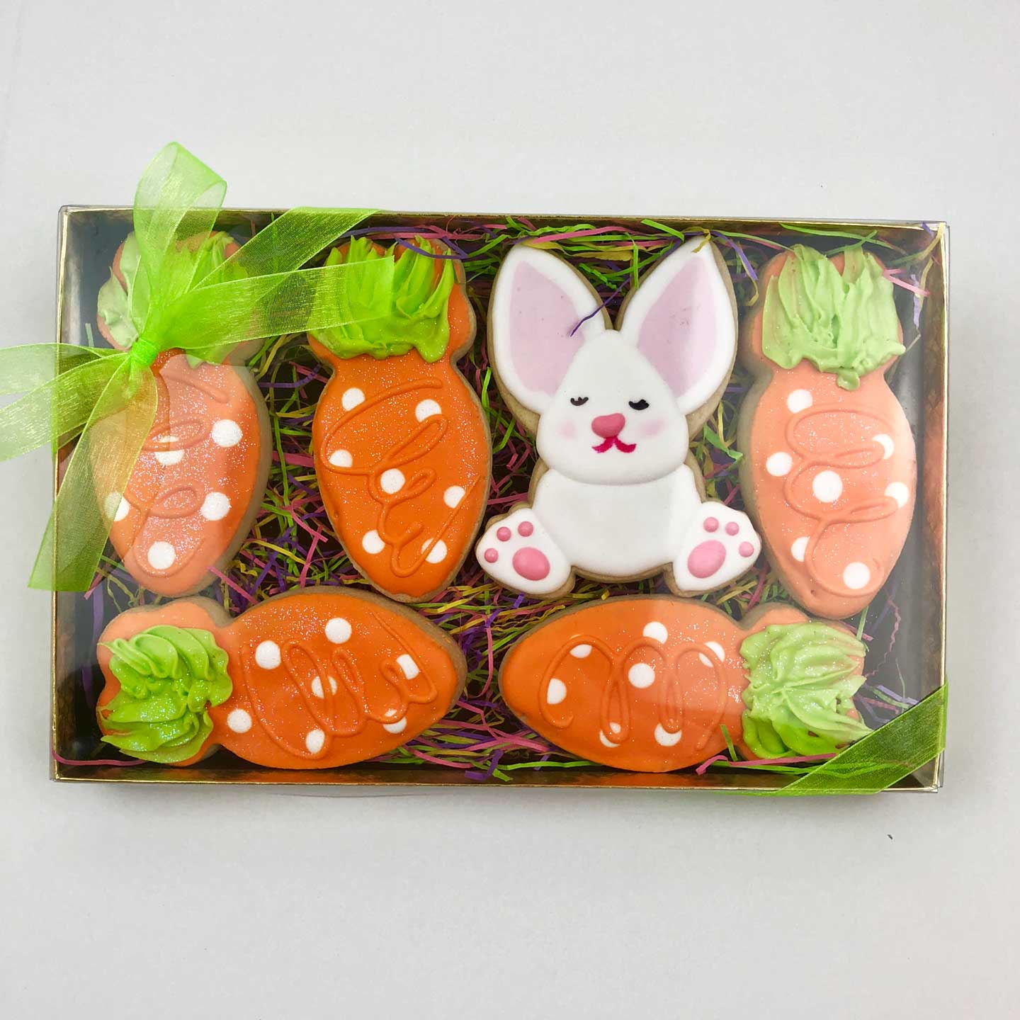 One white Bunny & five orange Carrot cookies with white dots in a box with a clear closed top and a green bow on the top left corner