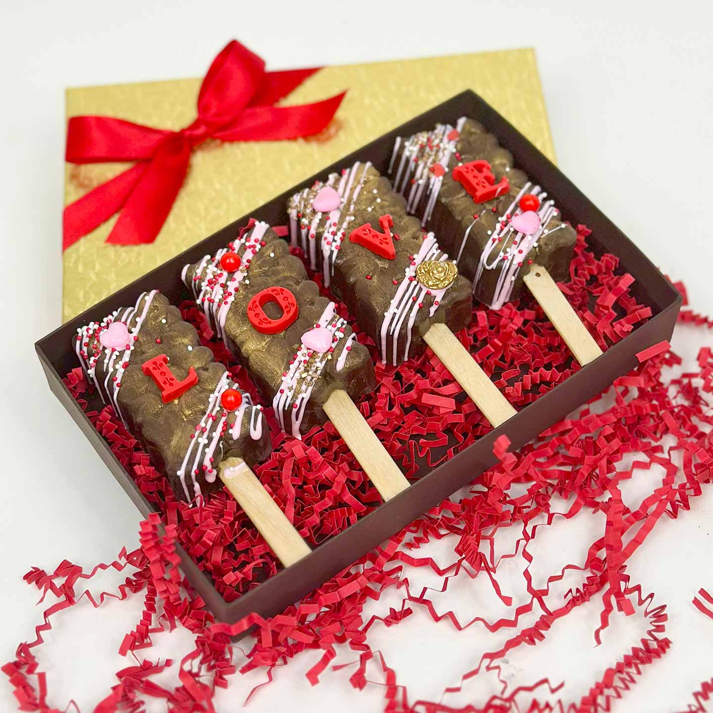 4 chocolate Cakesicles inside a box. Box top has a a satin bow.