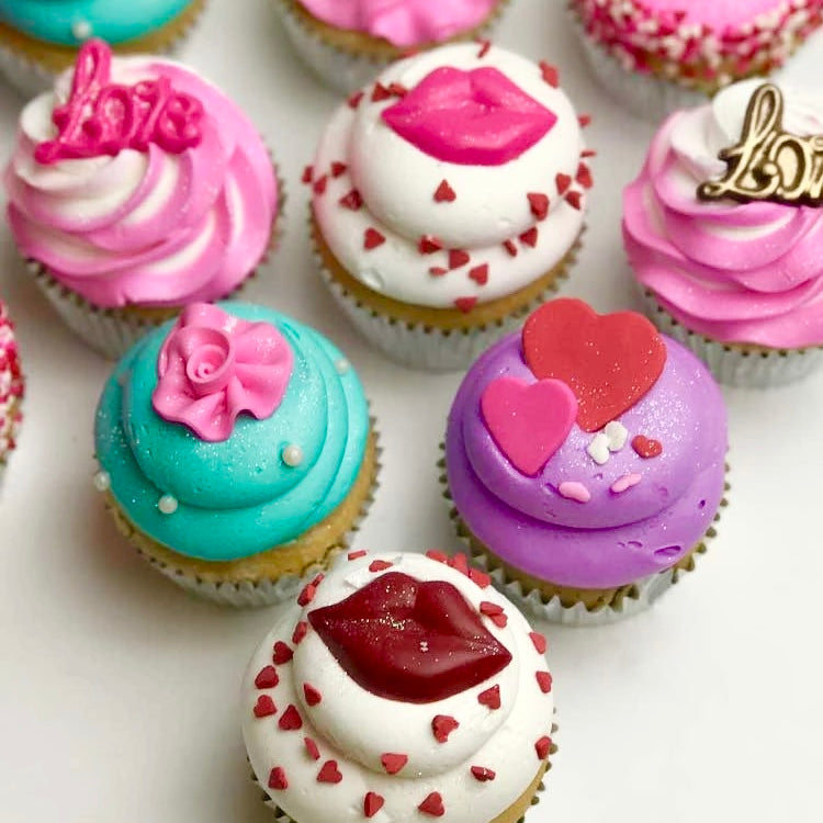 Pink, white, teal, and purple Valentine themed cupcakes, decorated with pink and red hearts, pink and red lips, pink and gold love and pink flower.