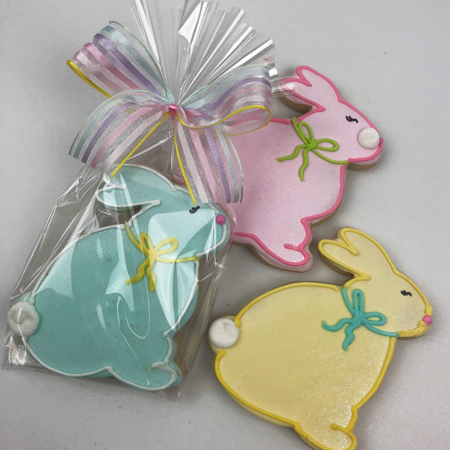 Blue, pink, and yellow Easter Bunny Cookies. The blue cookie is warped in cellophane with a ribbon