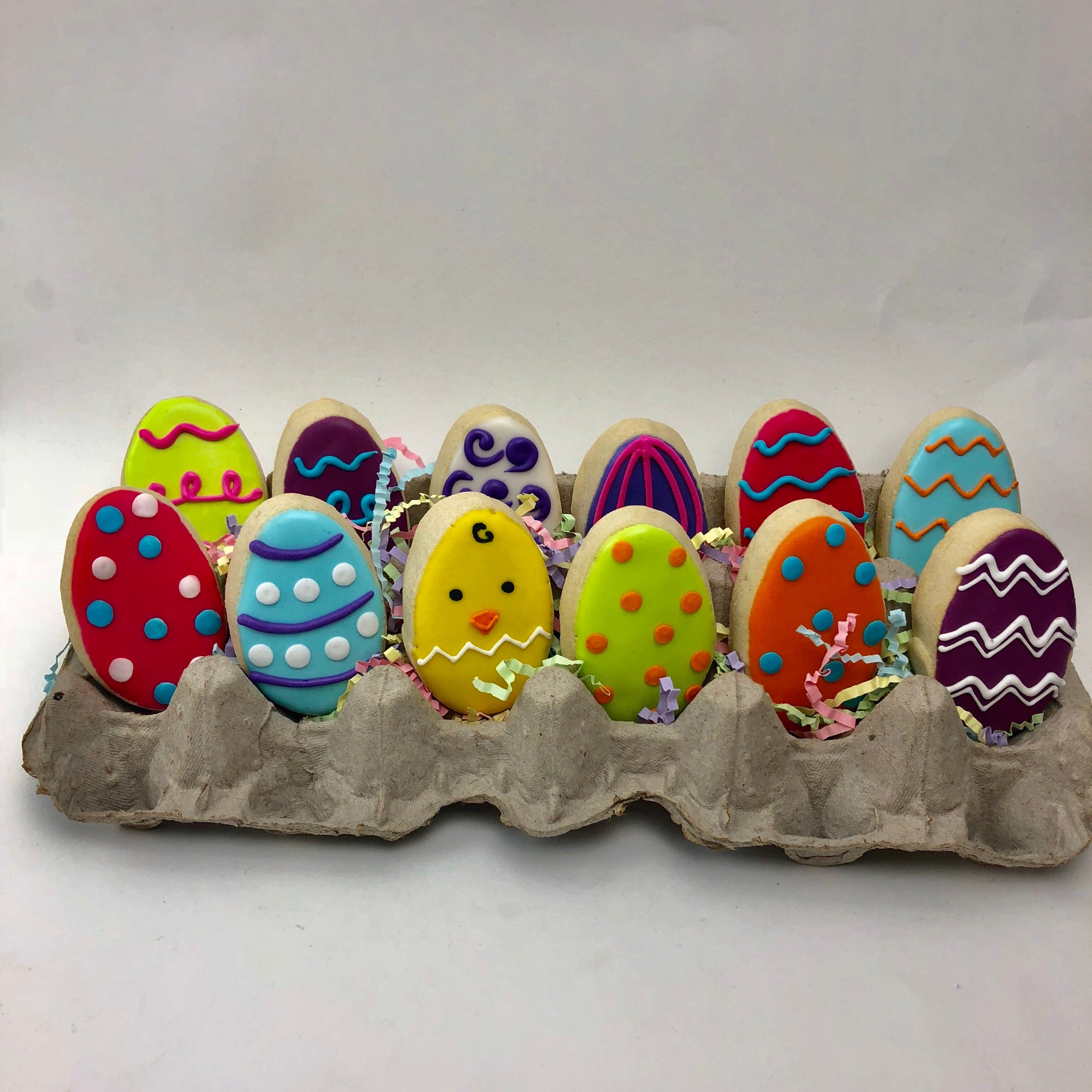 A dozen decorated Easter Egg Cookies in a carton