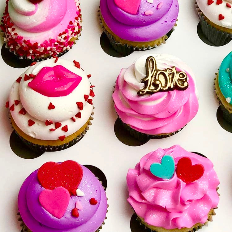 Pink, white, teal, and purple Valentine themed cupcakes, decorated with pink, red and teal hearts, pink and red lips, pink and gold love and pink flower.