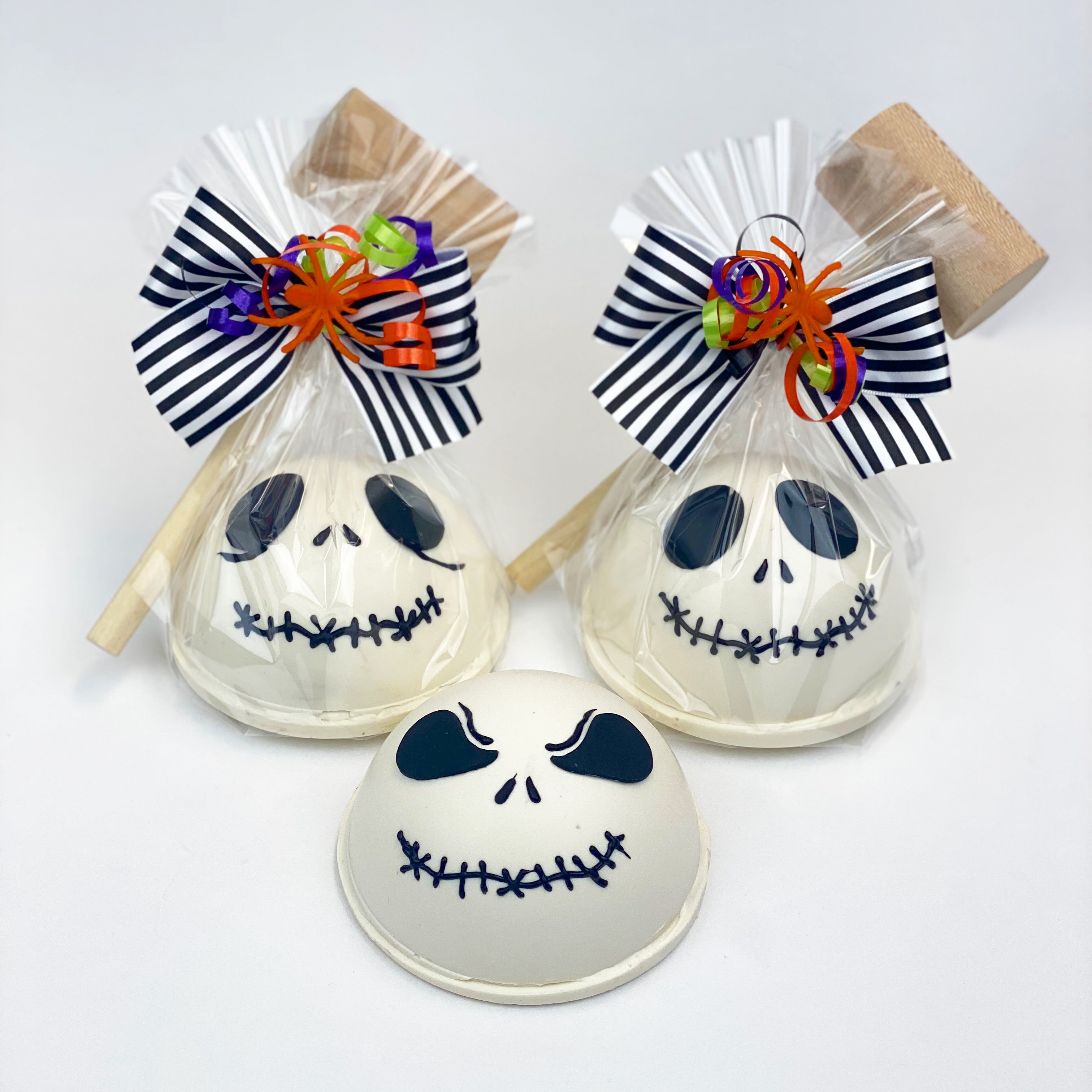 Three Jack Pinatas. Two are wrapped in clear cello and decorated with black, white, orange, green, and purple ribbons and have a mallet.