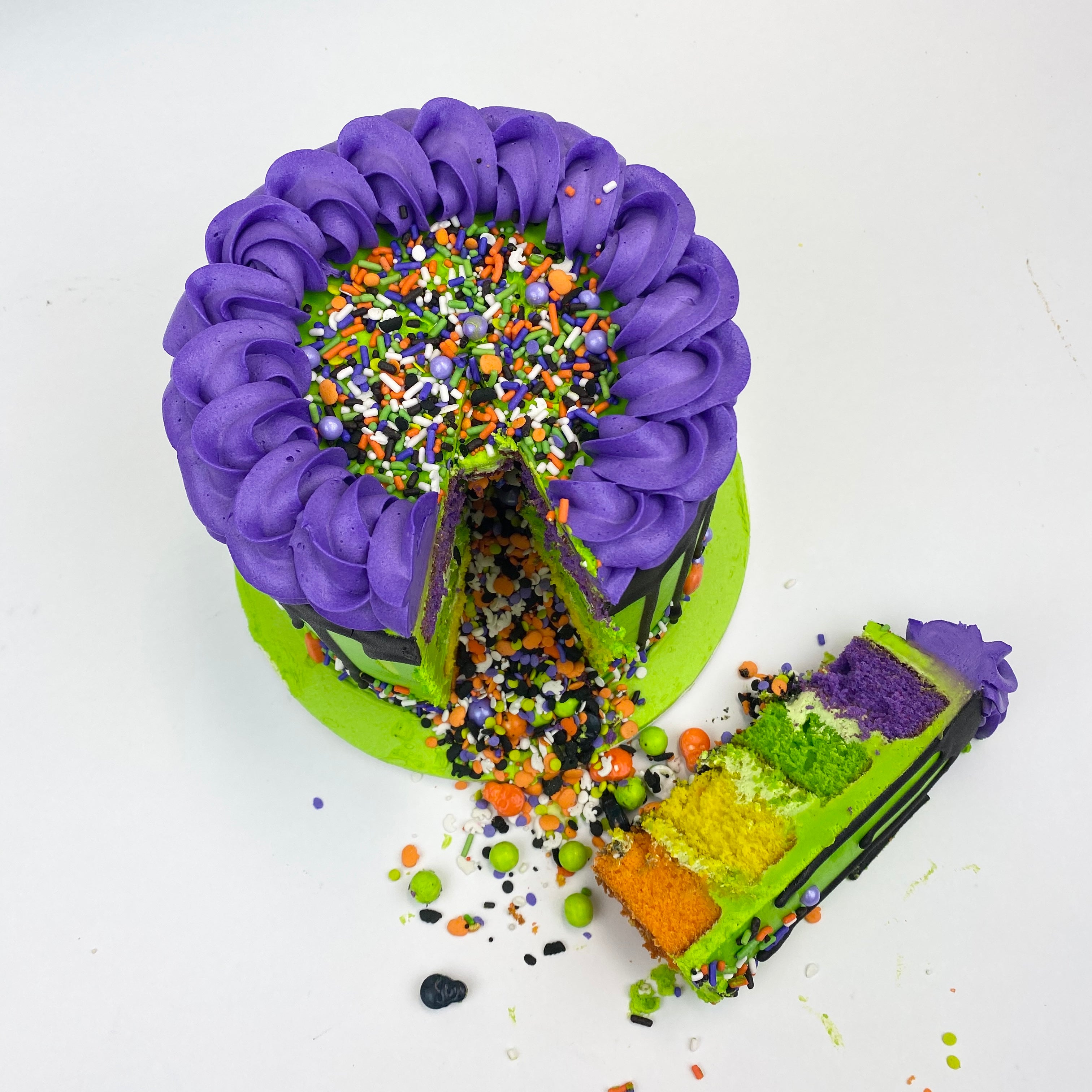 Green, purple, and black Halloween Pinata Cake, cut open with colorful candy coming out of it