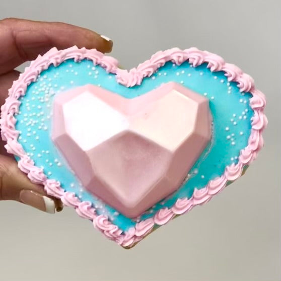 A pink geode chocolate heart on a blue heart-shaped base with pink icing around the edge of the base.